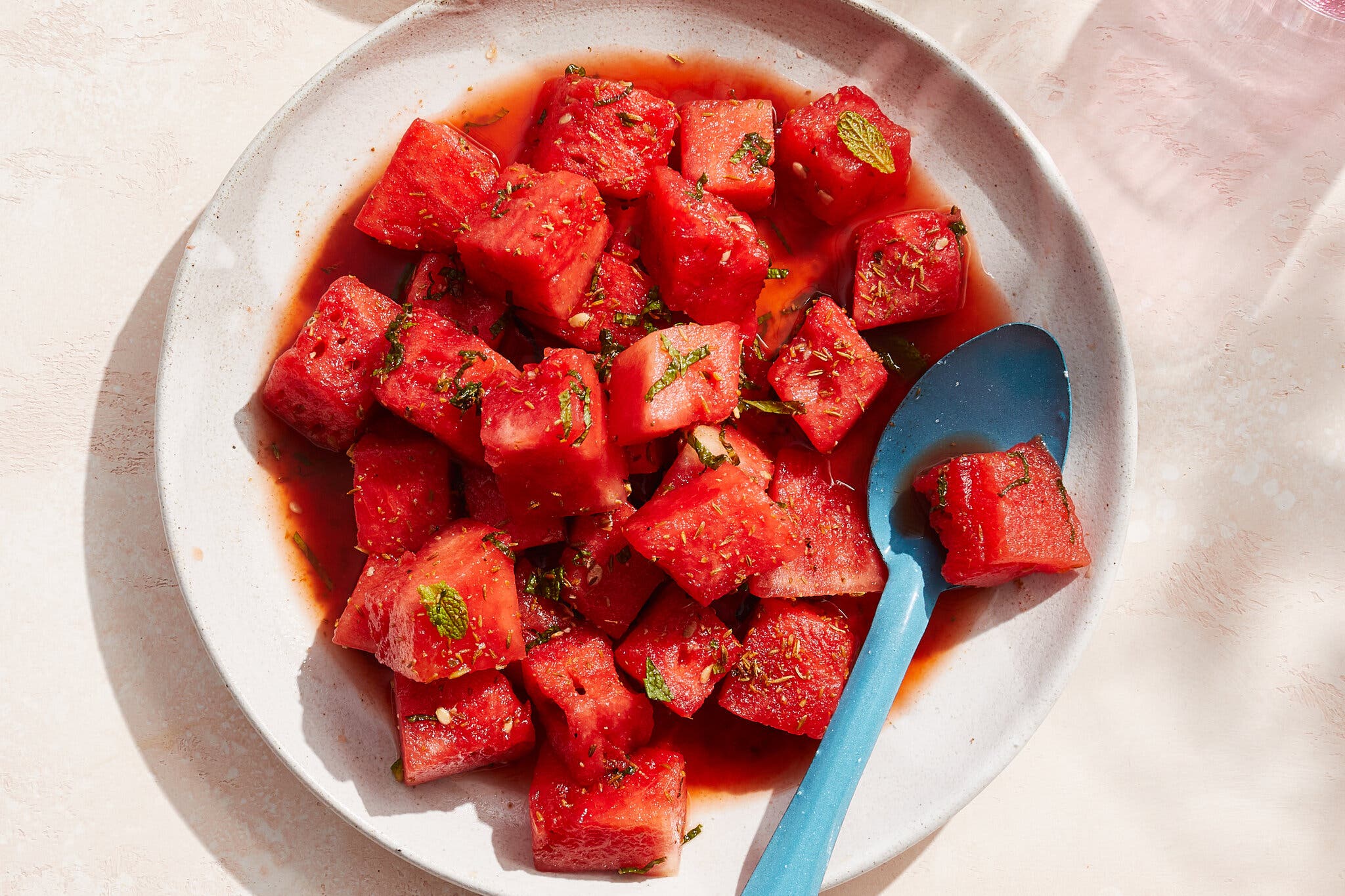 Cubed watermelon sits on a white plate against a light pink background.