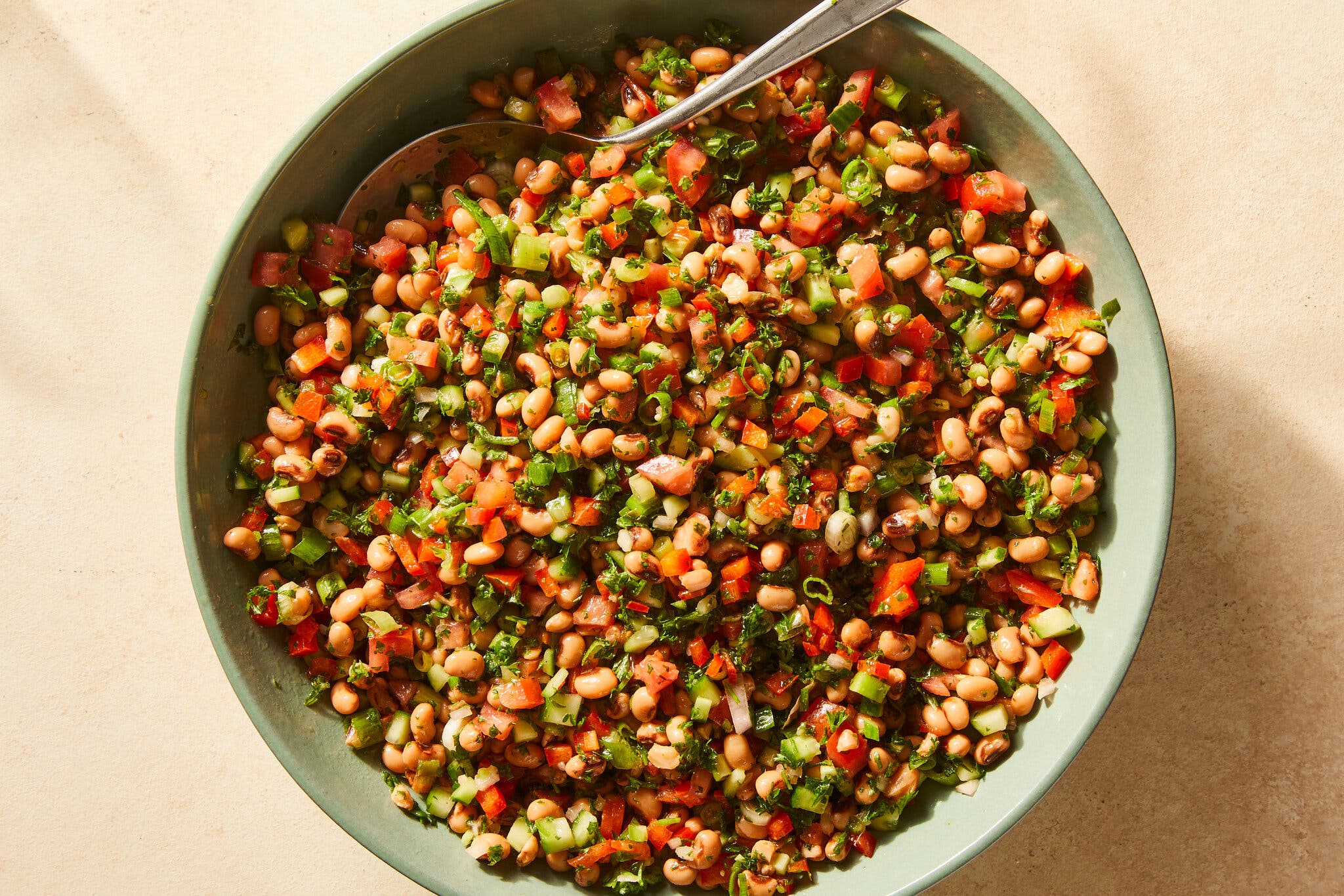 A vibrant salad of black-eyed peas, tomato, cucumbers, bell peppers, chiles and herbs fill a sea foam green serving bowl.