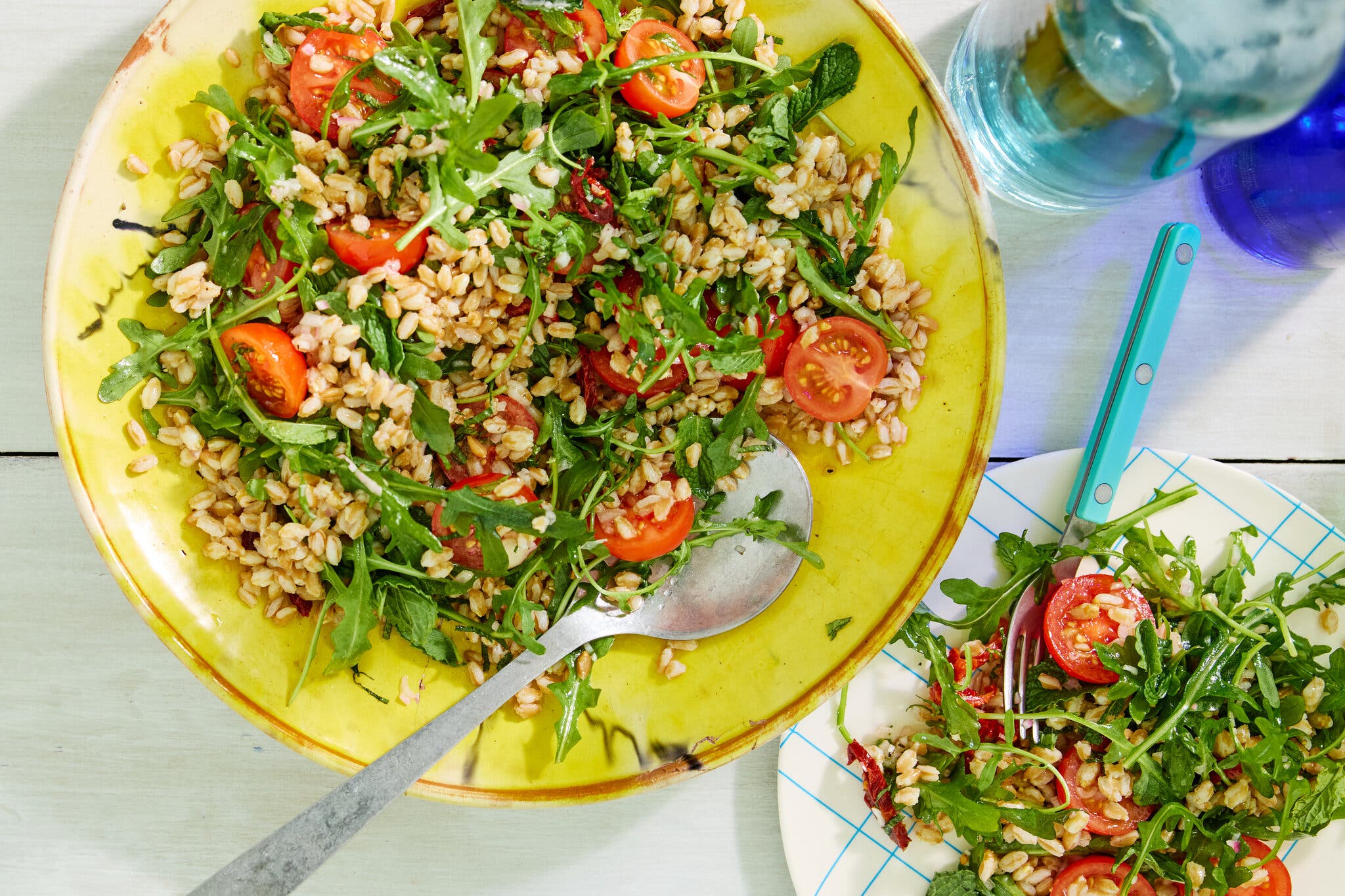 An overhead image of a farro and tomato salad topped with arugula on a wooden table.