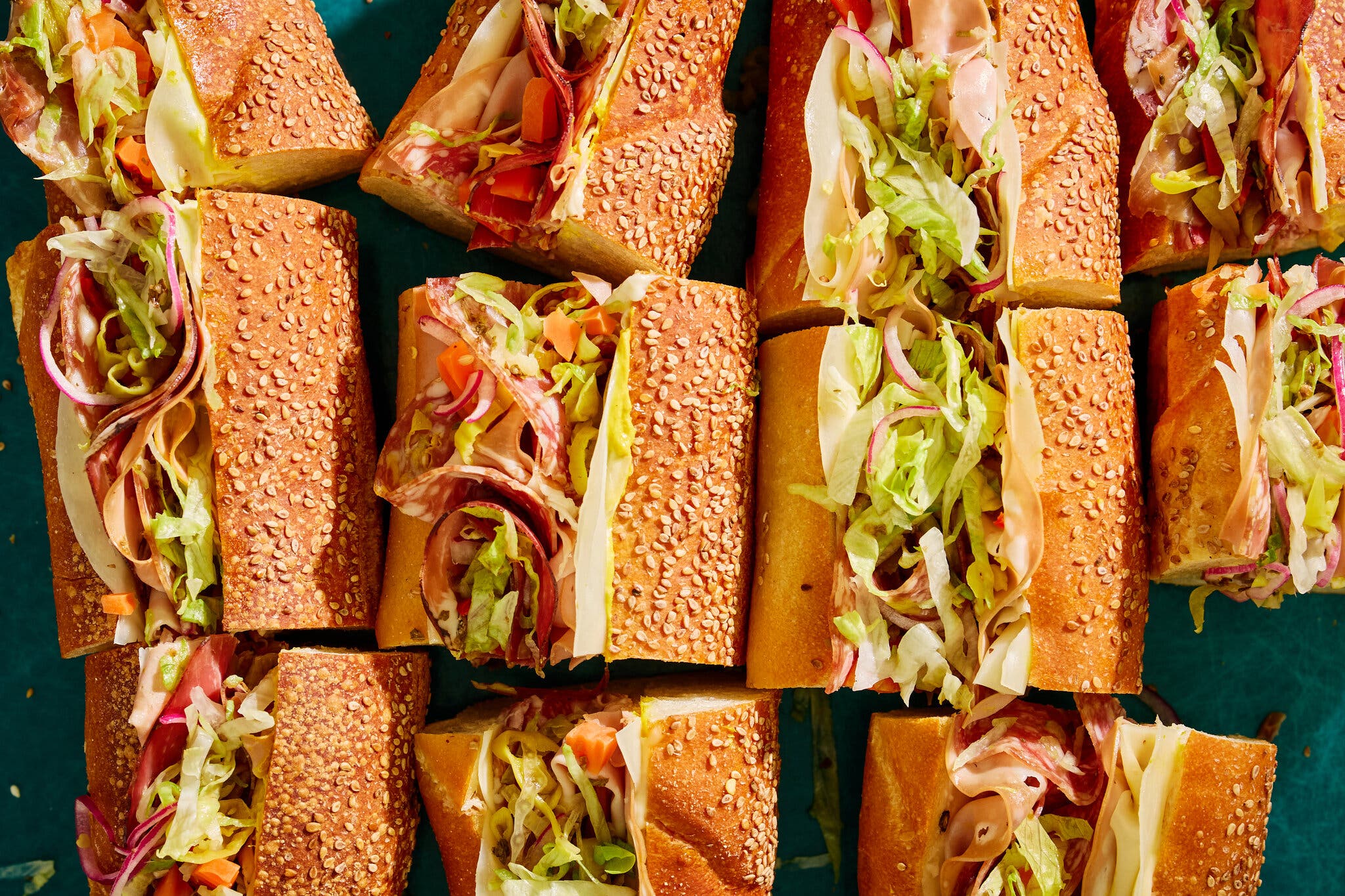 Quarters of an Italian hero stuffed with deli meats, cheese and seasoned lettuce fill a serving board.