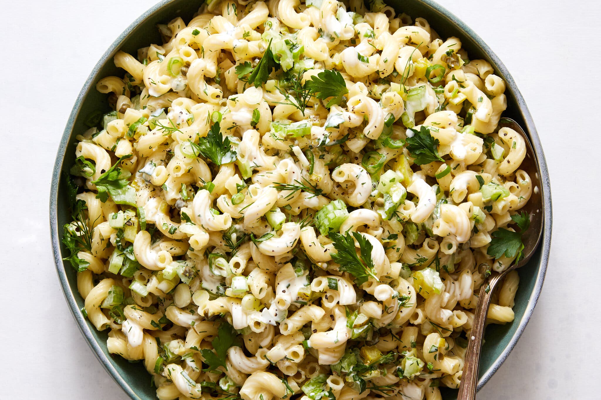 An overhead image shows a pasta salad of macaroni, celery and herbs tossed in a light creamy dressing.