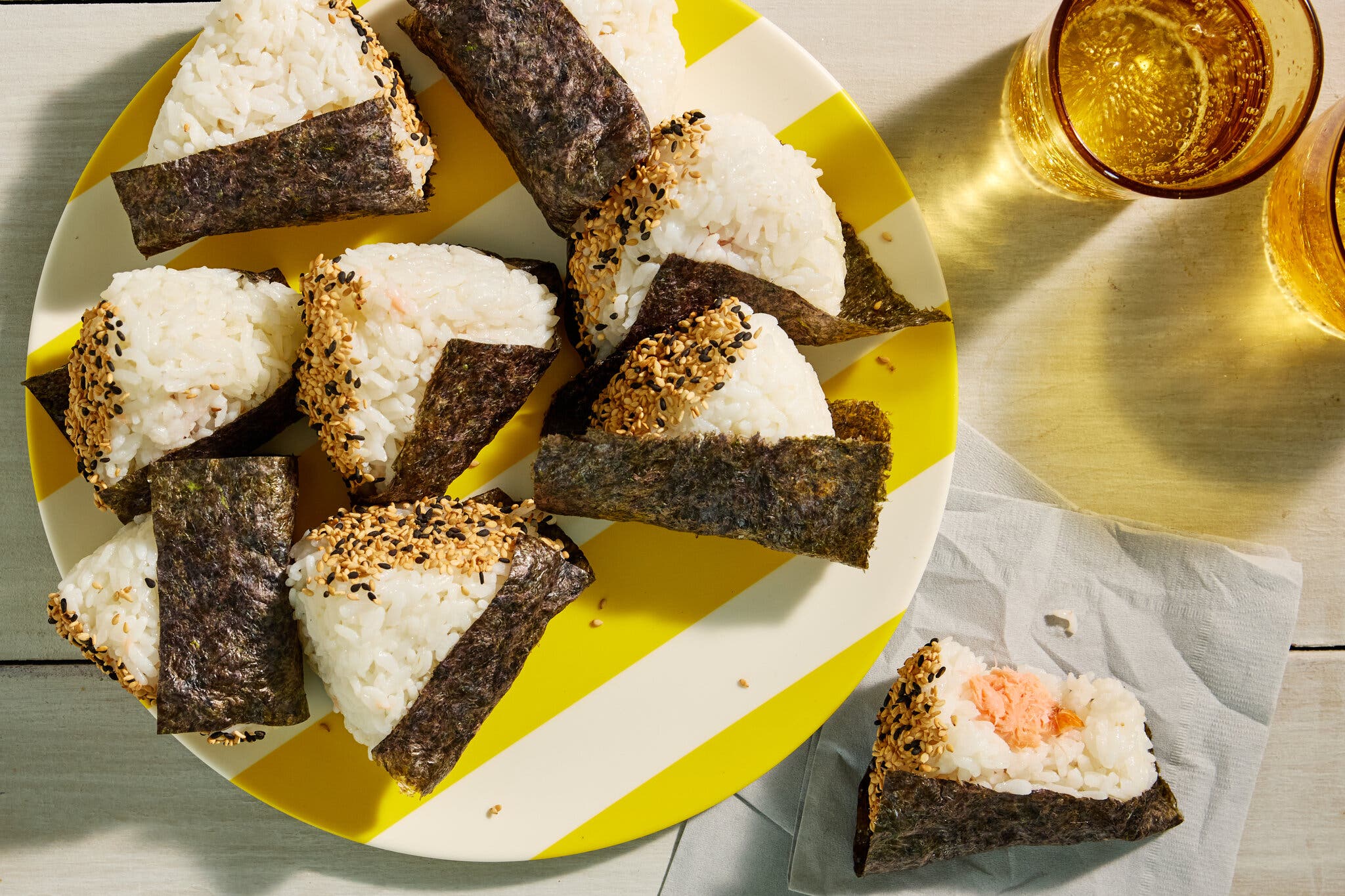 Onigiri with their sides dipped in mixed sesame seeds sit on a white and yellow striped plate on a wooden table.