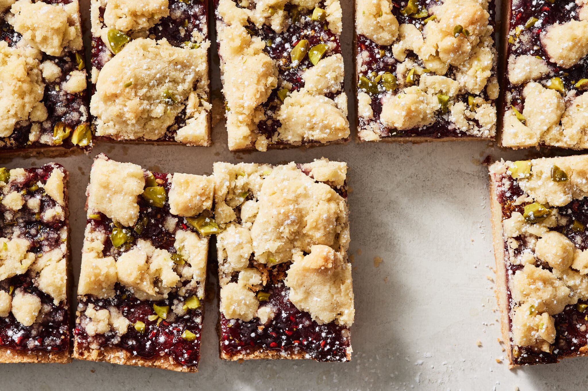 Jammy bars topped with pistachio are photographed from overhead.