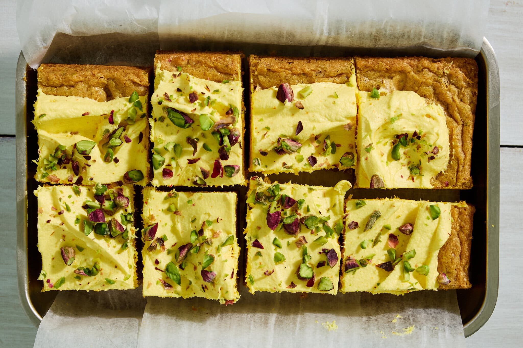 An overhead image of blondies frosted with a yellow frosting and scattered with pistachios.