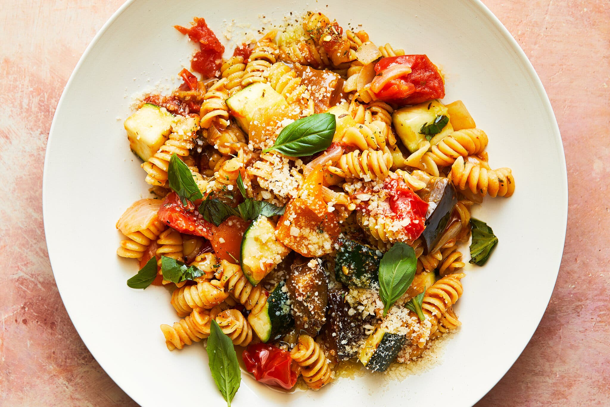 An overhead image of short, curly pasta sauced and tossed with various summer vegetables. It’s all finished with a sprinkle of basil and cheese.