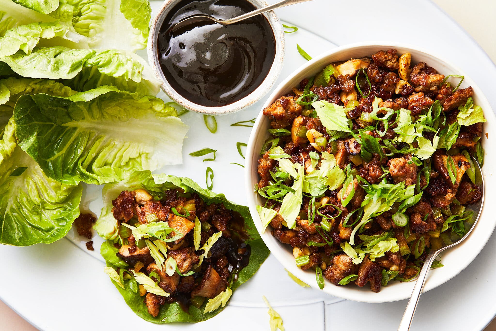 An overhead image of lettuce cups filled with ground turkey and herbs. More lettuce sits to the side next to a dark sauce.