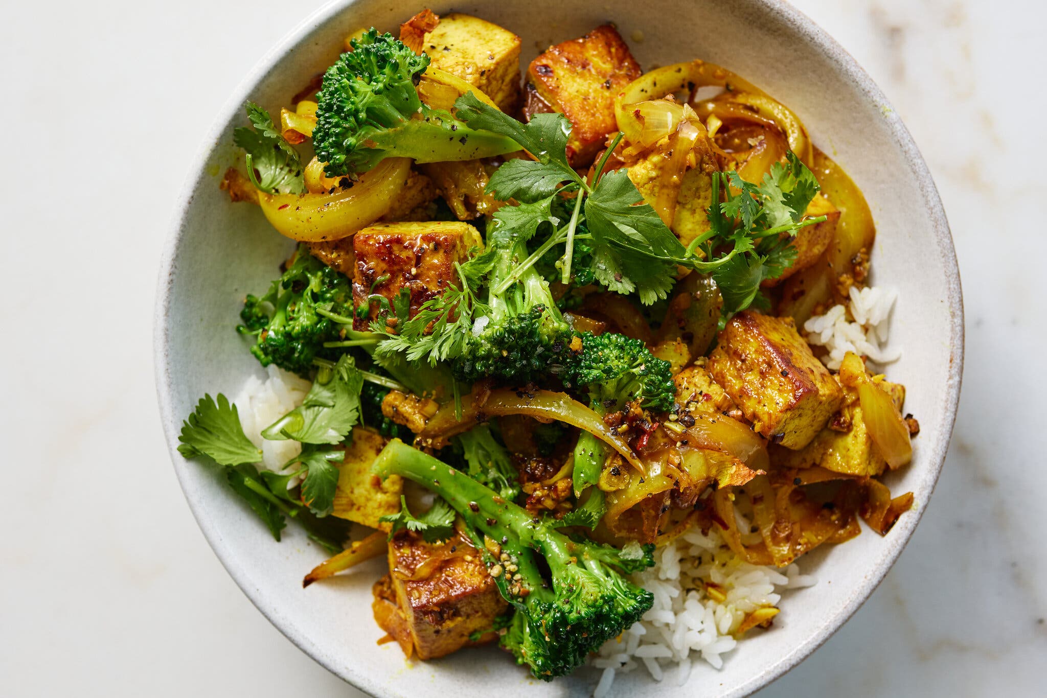 Golden tofu and broccoli stems topped with herbs sit on a bed of rice.