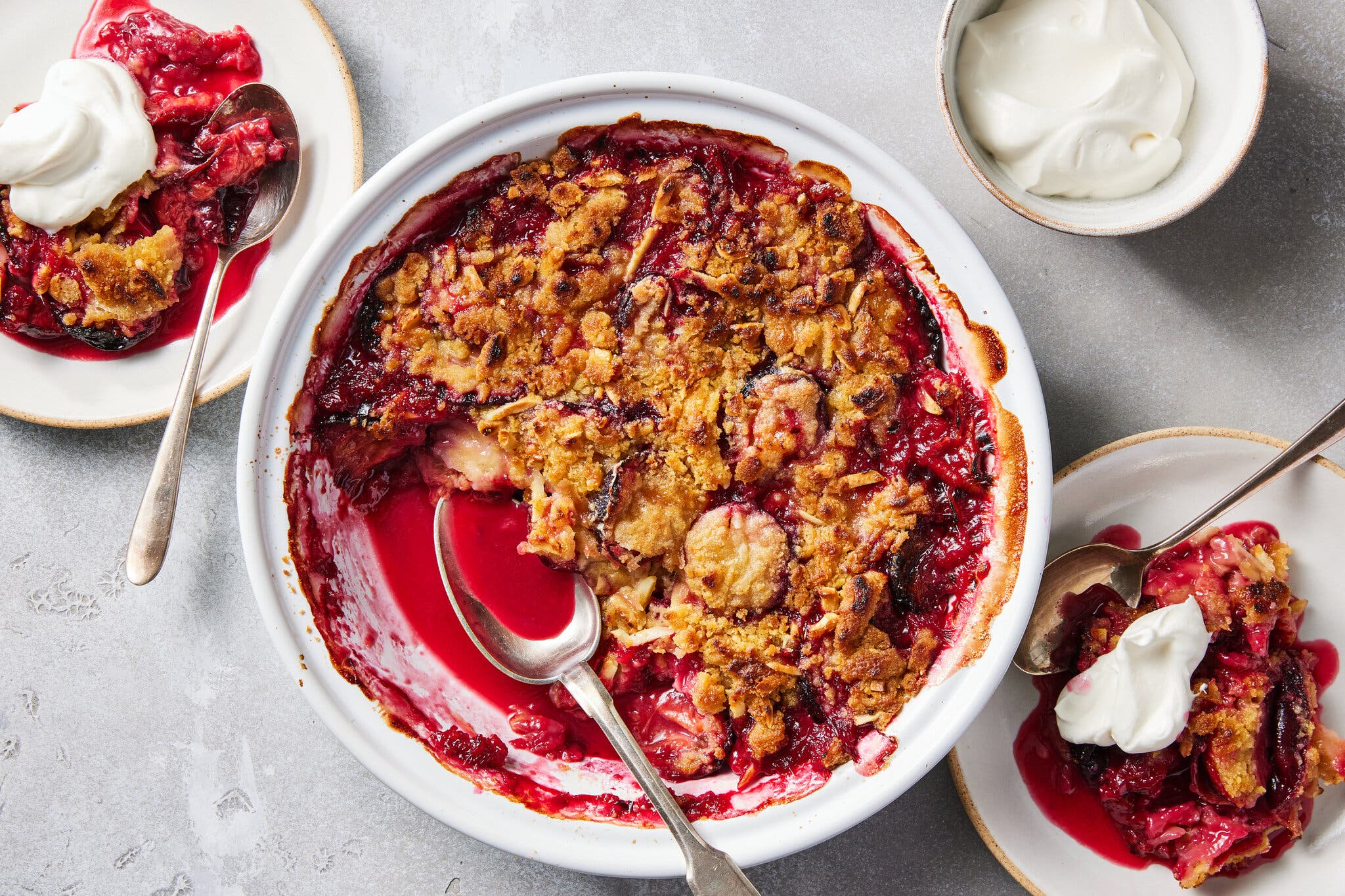 An overhead image of a plum crumble in a baking dish next to two servings.