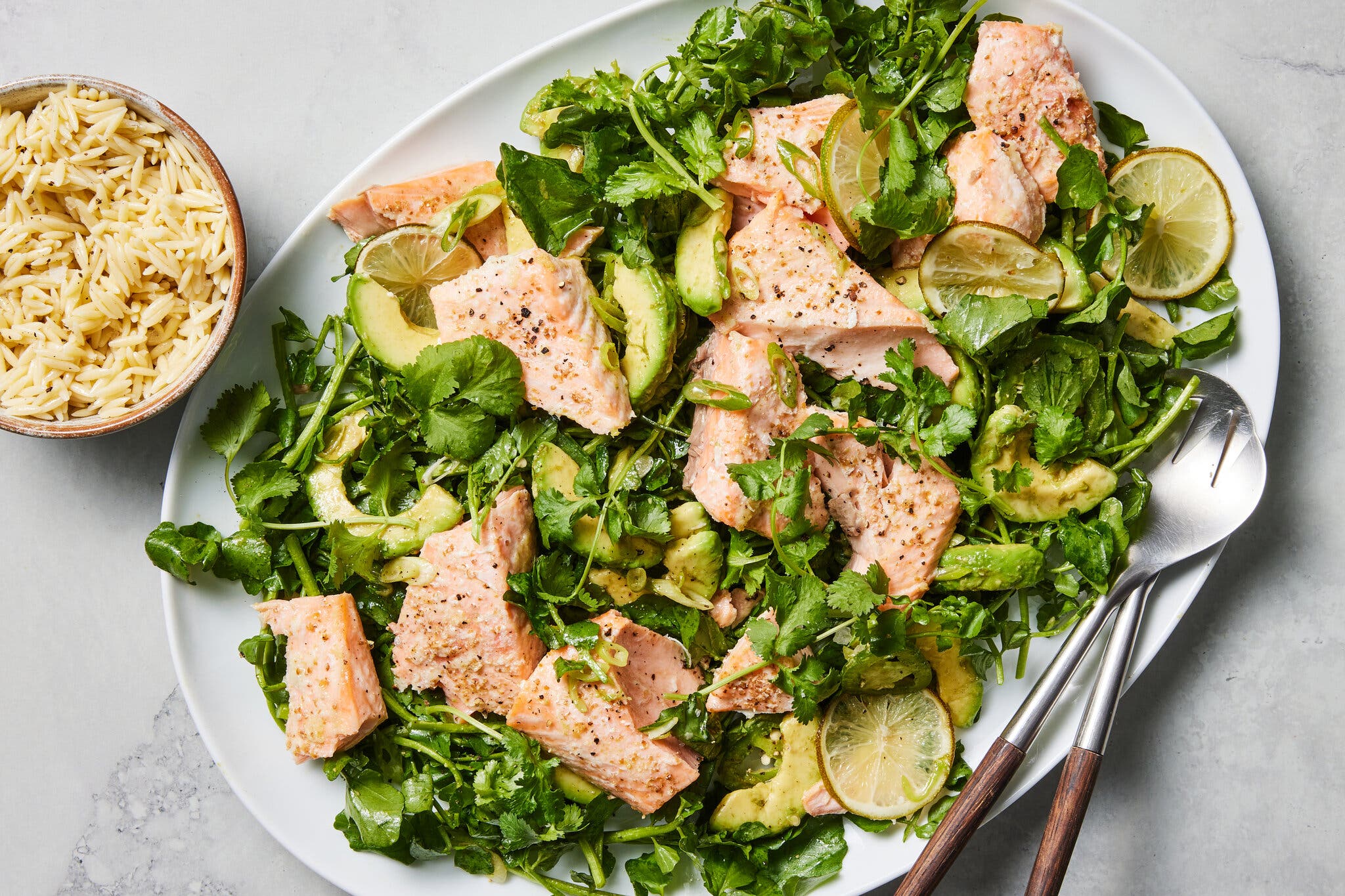 Salmon chunks and avocado slices sit on a bed of cilantro and watercress.