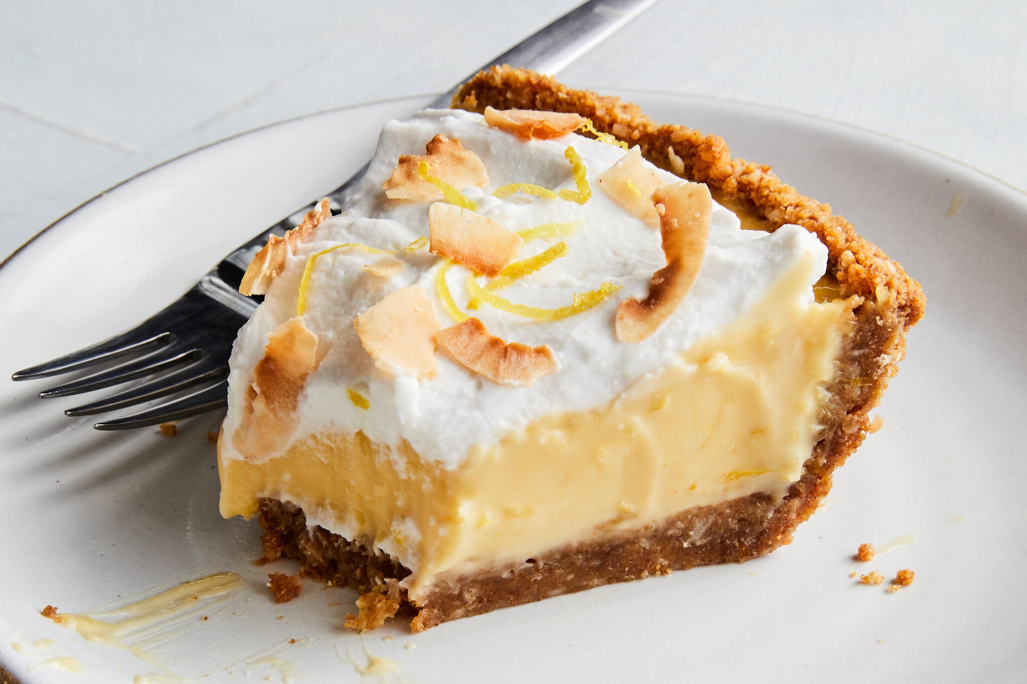 A side image of a pie with a graham cracker crust and a lemony layer topped with whipped cream and toasted coconut.