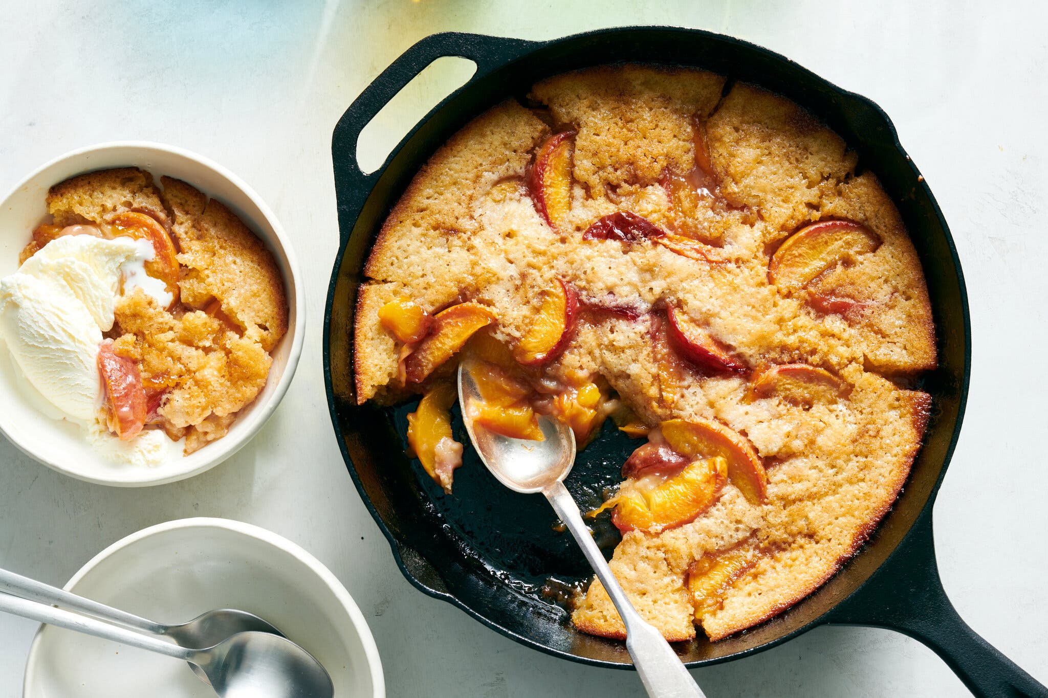 An overhead image of a buttermilk cake topped with peach slices in a cast-iron skillet. A single serving sits to the left.
