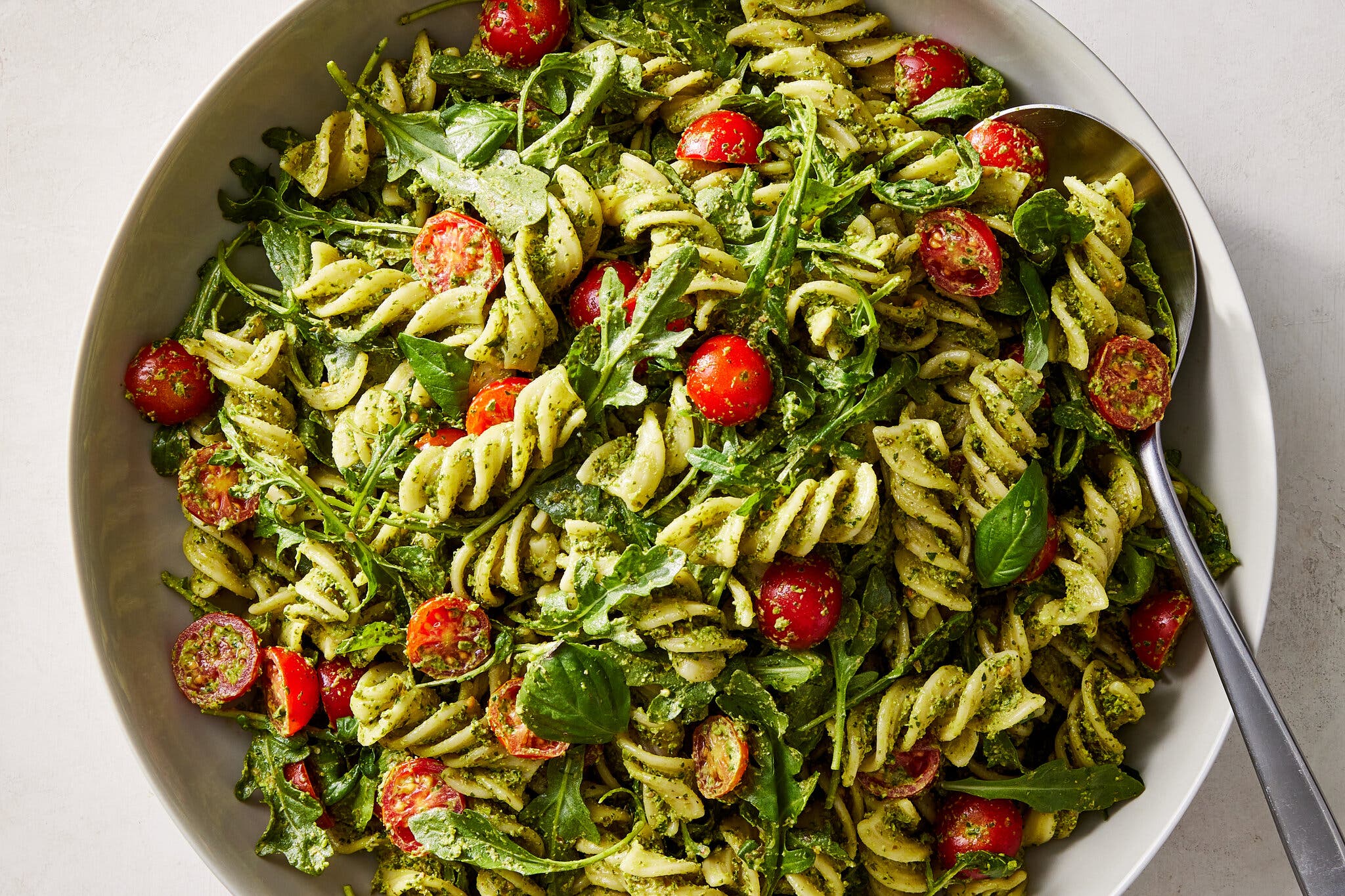 Short curly pasta coated in a green pesto is studded with halved tomatoes.