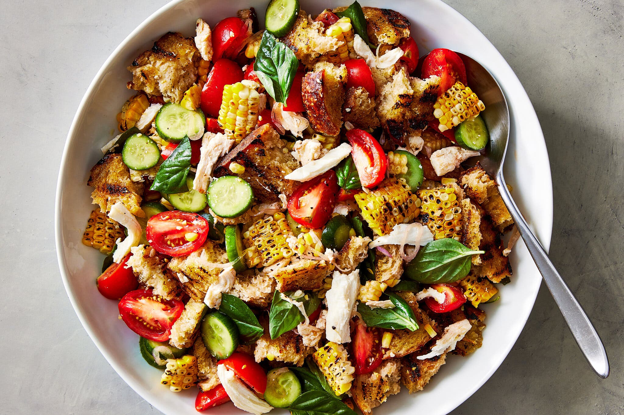 Chunks of bread, quartered tomatoes and charred bits of corn fill a white bowl.