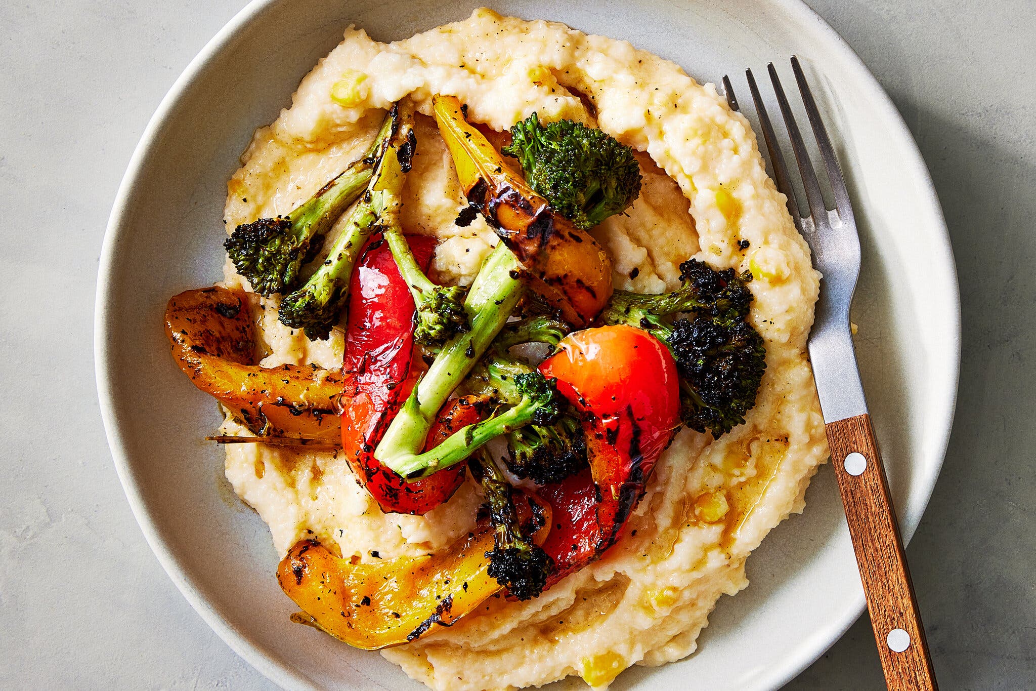 Charred broccoli and peppers top creamy grits in a white bowl.
