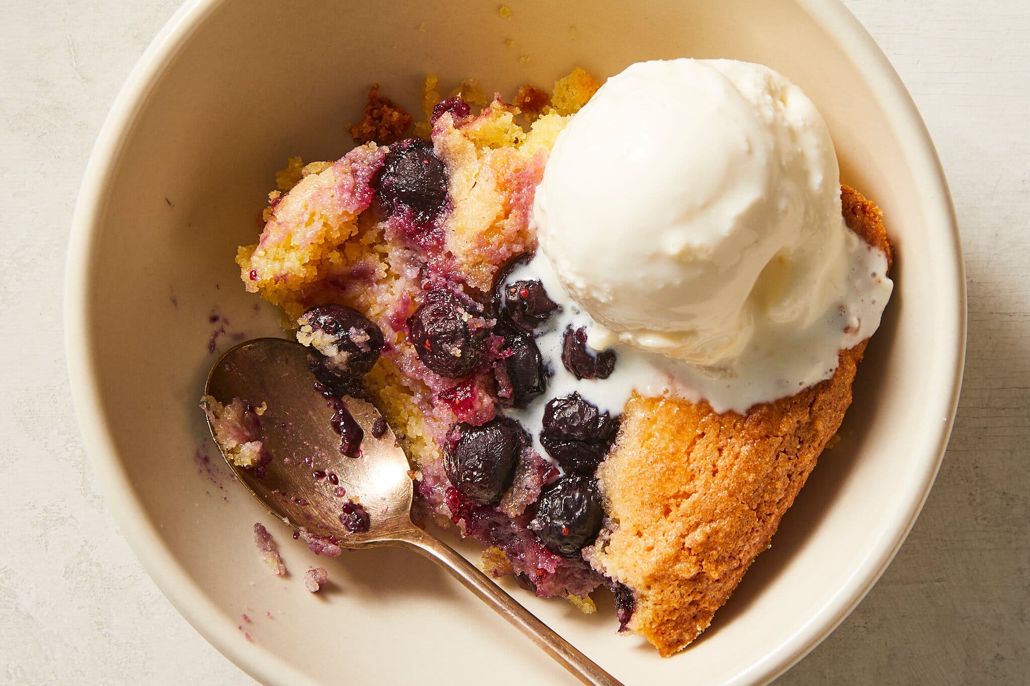An overhead image of a bowl filled with blueberry spoon cake topped with a scoop of ice cream.