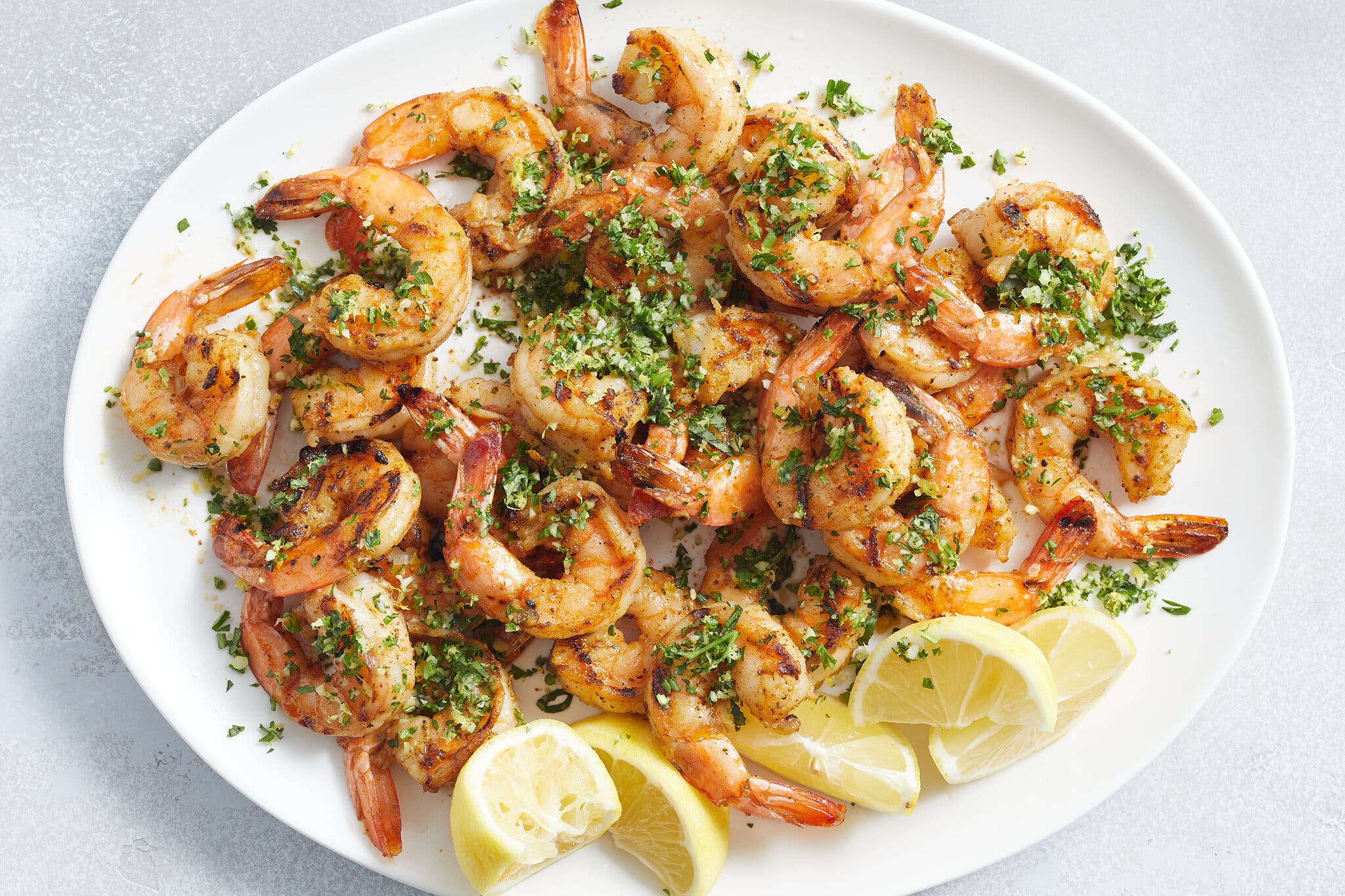 Grilled shrimp topped with herbs next to some spent lemon wedges on a white platter.