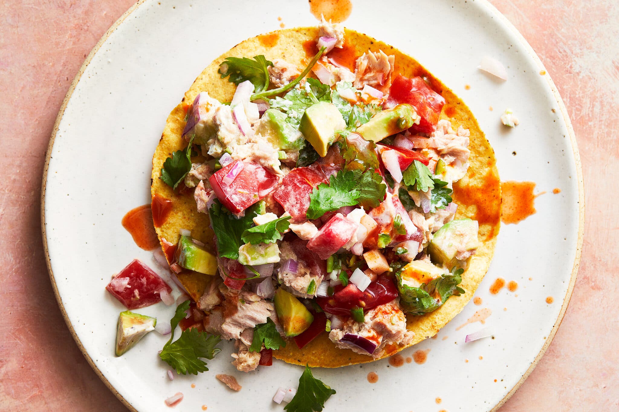 A tostada topped with spicy tuna and avocado sits on a white plate.