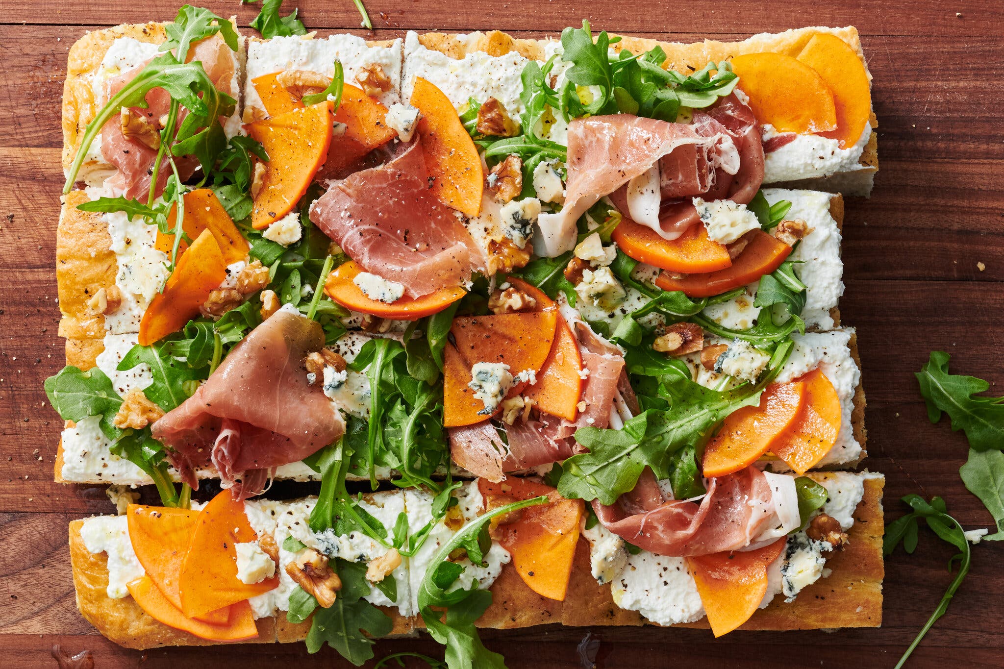 A slab of focaccia is topped with ricotta, vegetables and prosciutto.