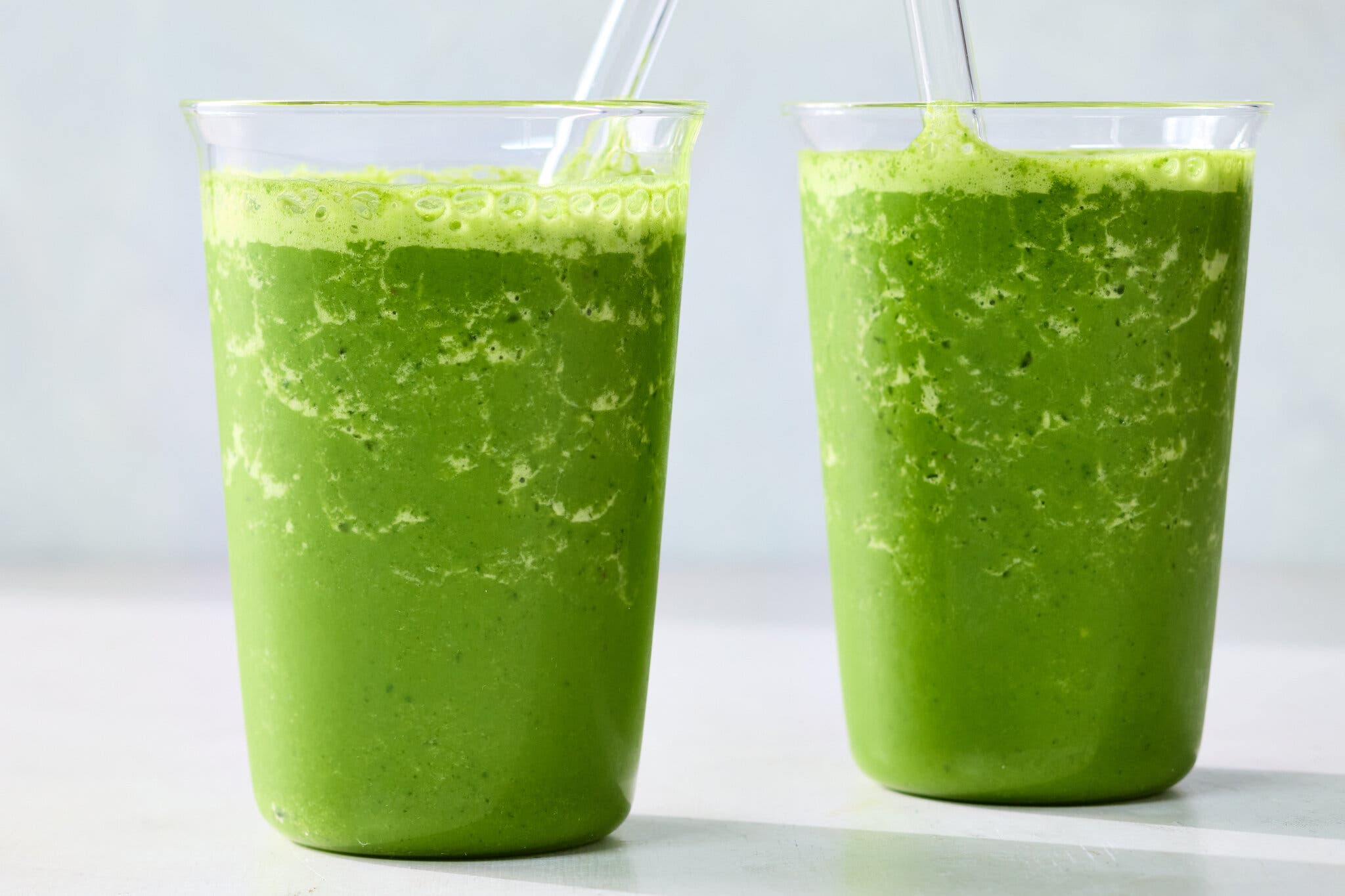 Two tall glasses are filled with a bright green liquid.