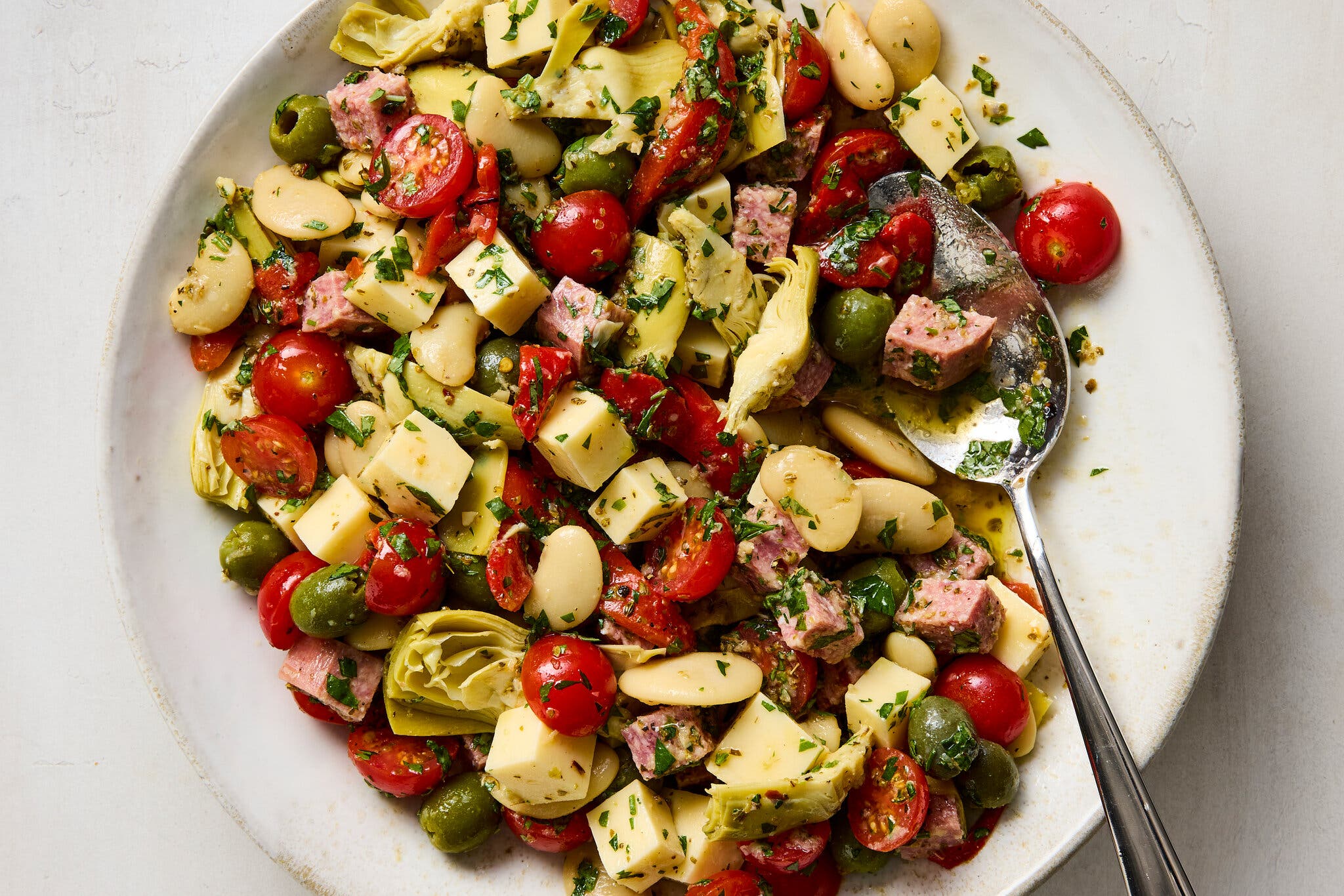 Artichoke hearts, beans, halved cherry peppers and chunks of cured meat on a white platter.