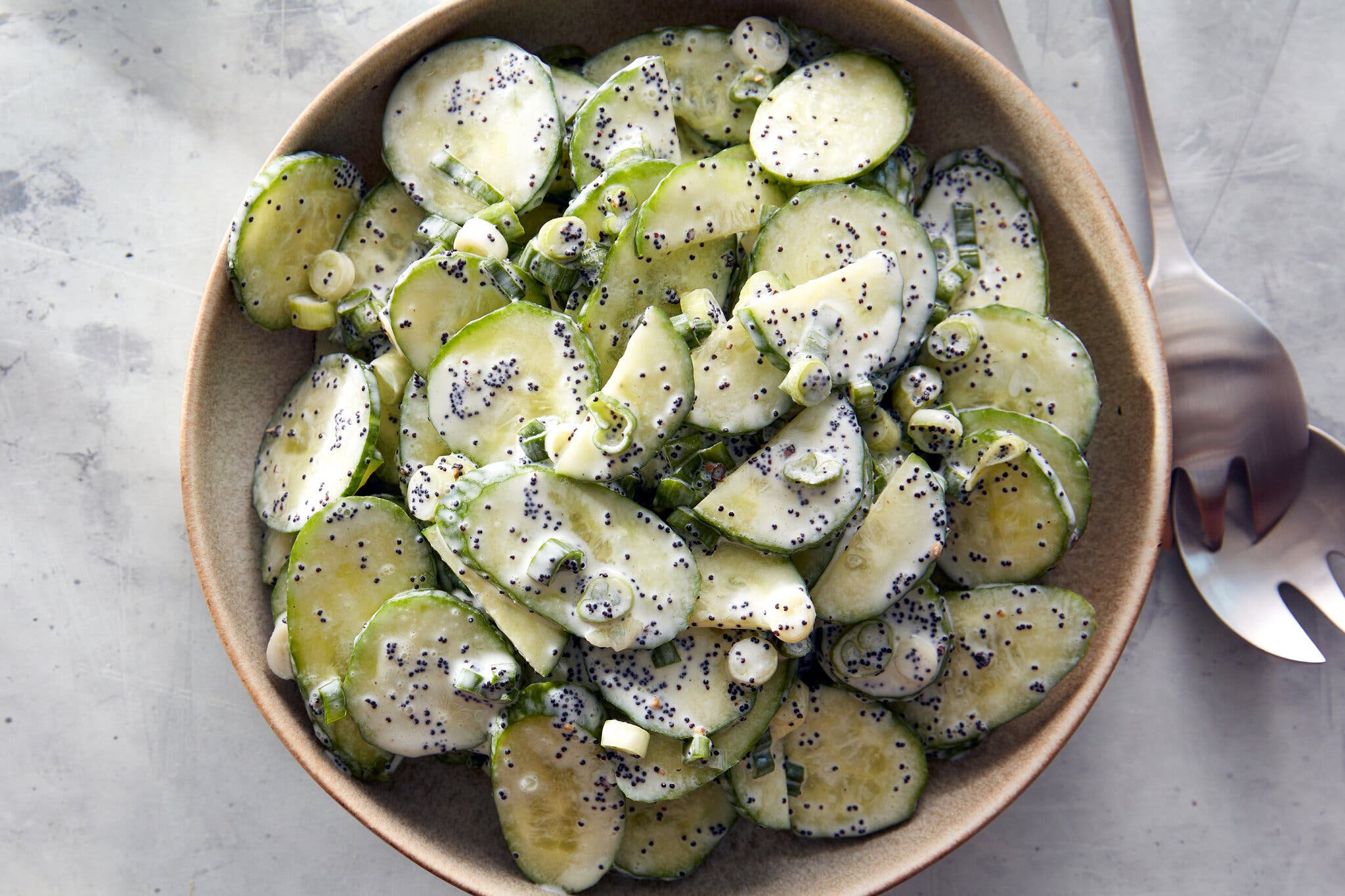 An overhead image of sliced cucumbers coated with a creamy sauce and speckled with poppy seeds.