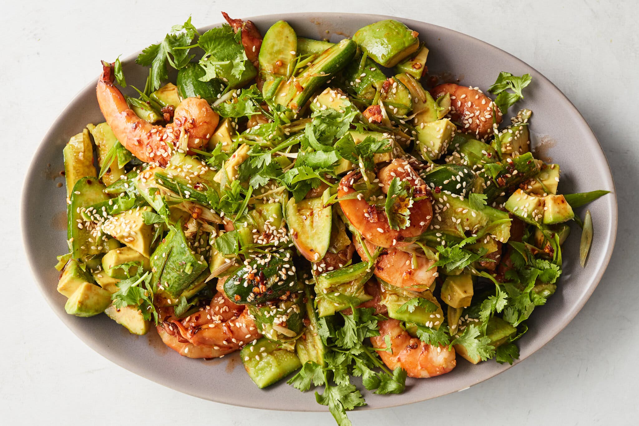 An overhead image of a platter topped with cucumbers, shrimp and avocado.