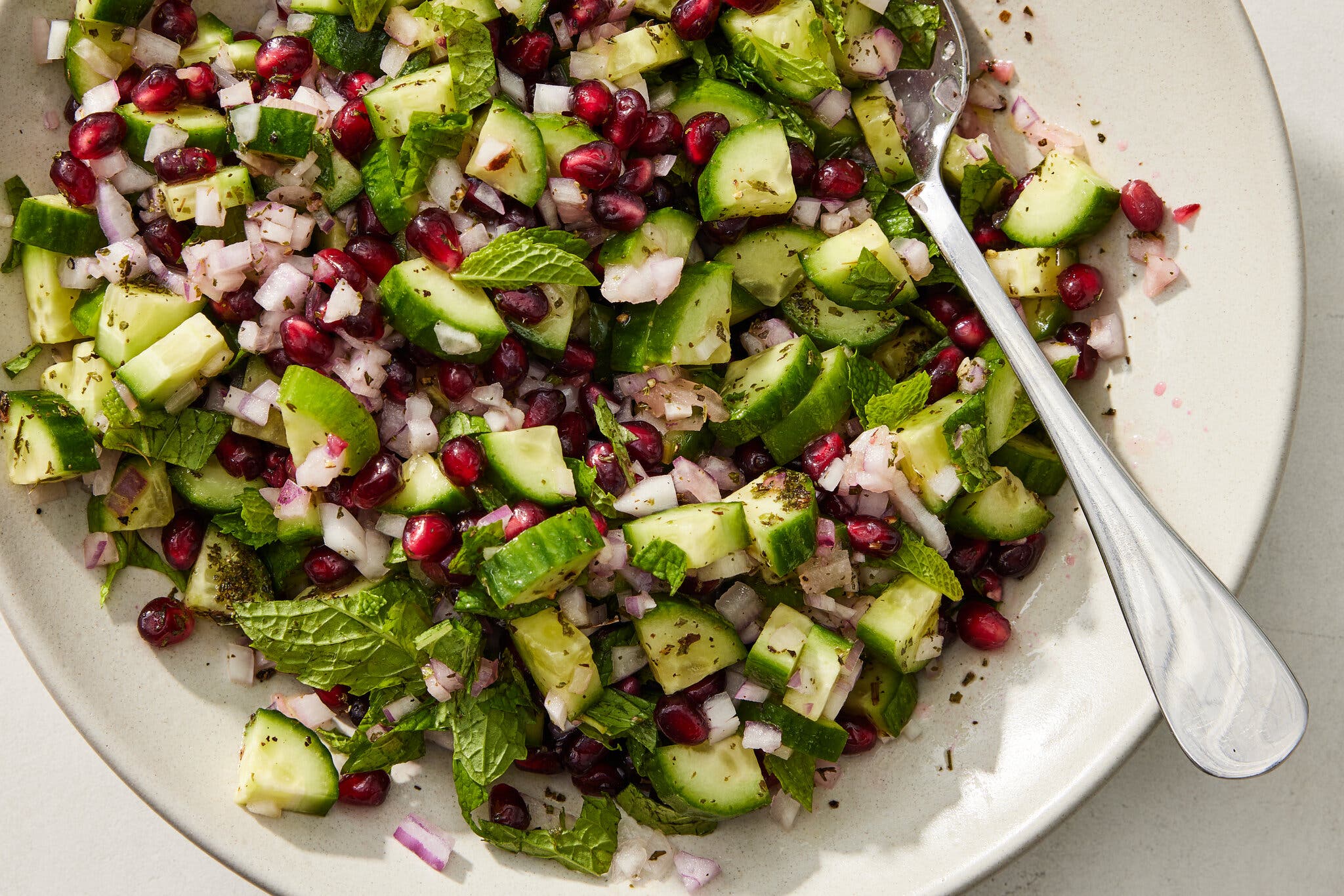 An overhead image of a platter of cubed cucumbers and pomegranate seeds.