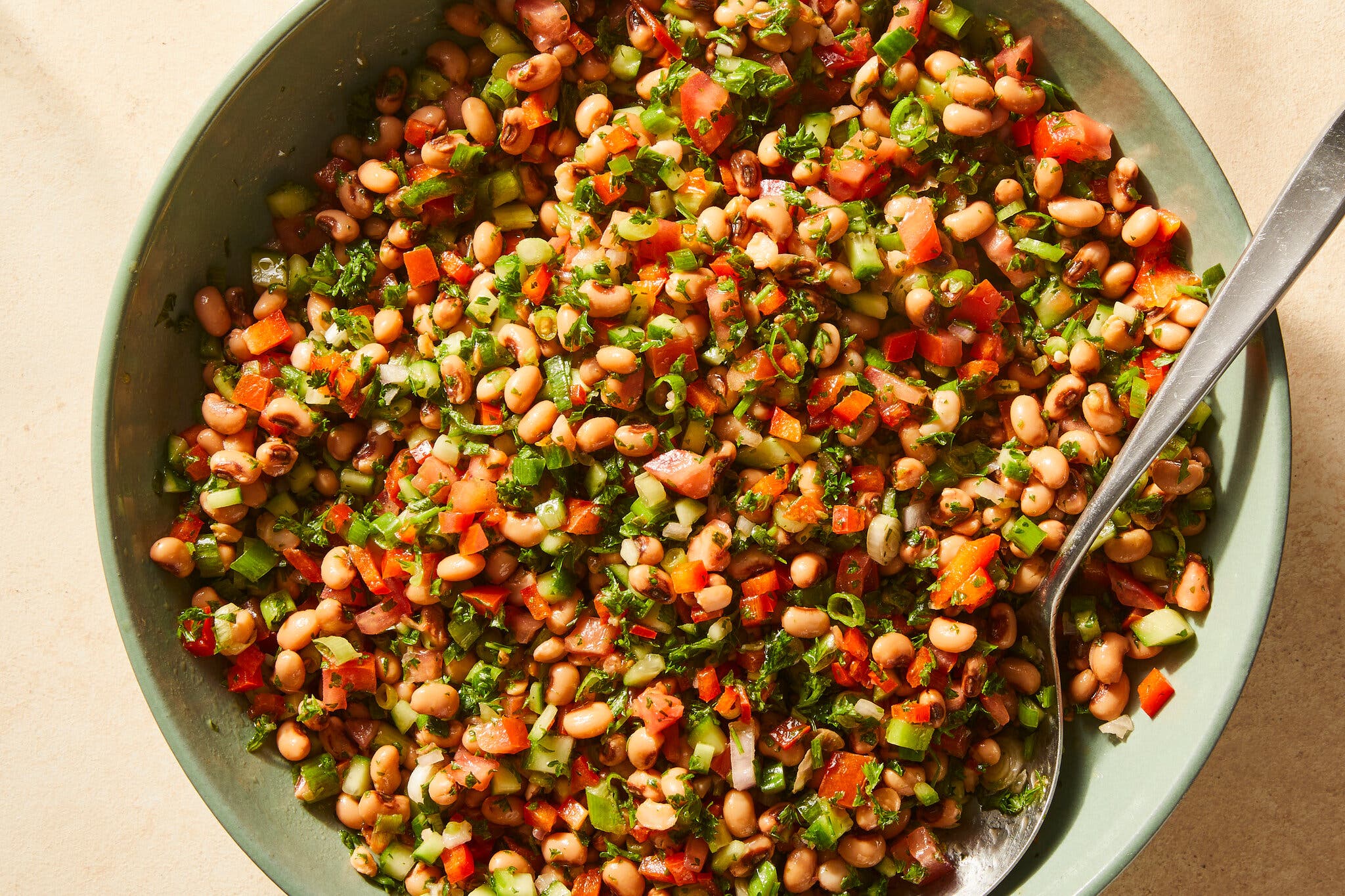 An overhead image of a large bowl filled with black-eyed peas, cucumbers, tomatoes and herbs.