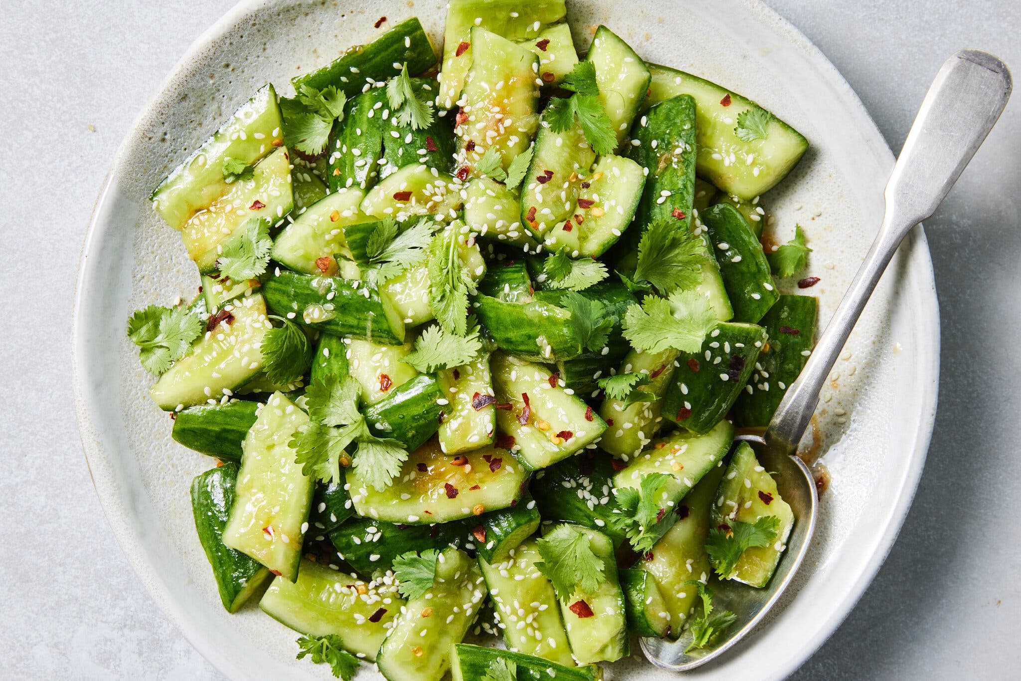 An overhead image of smashed cucumbers finished with cilantro and sesame seeds.