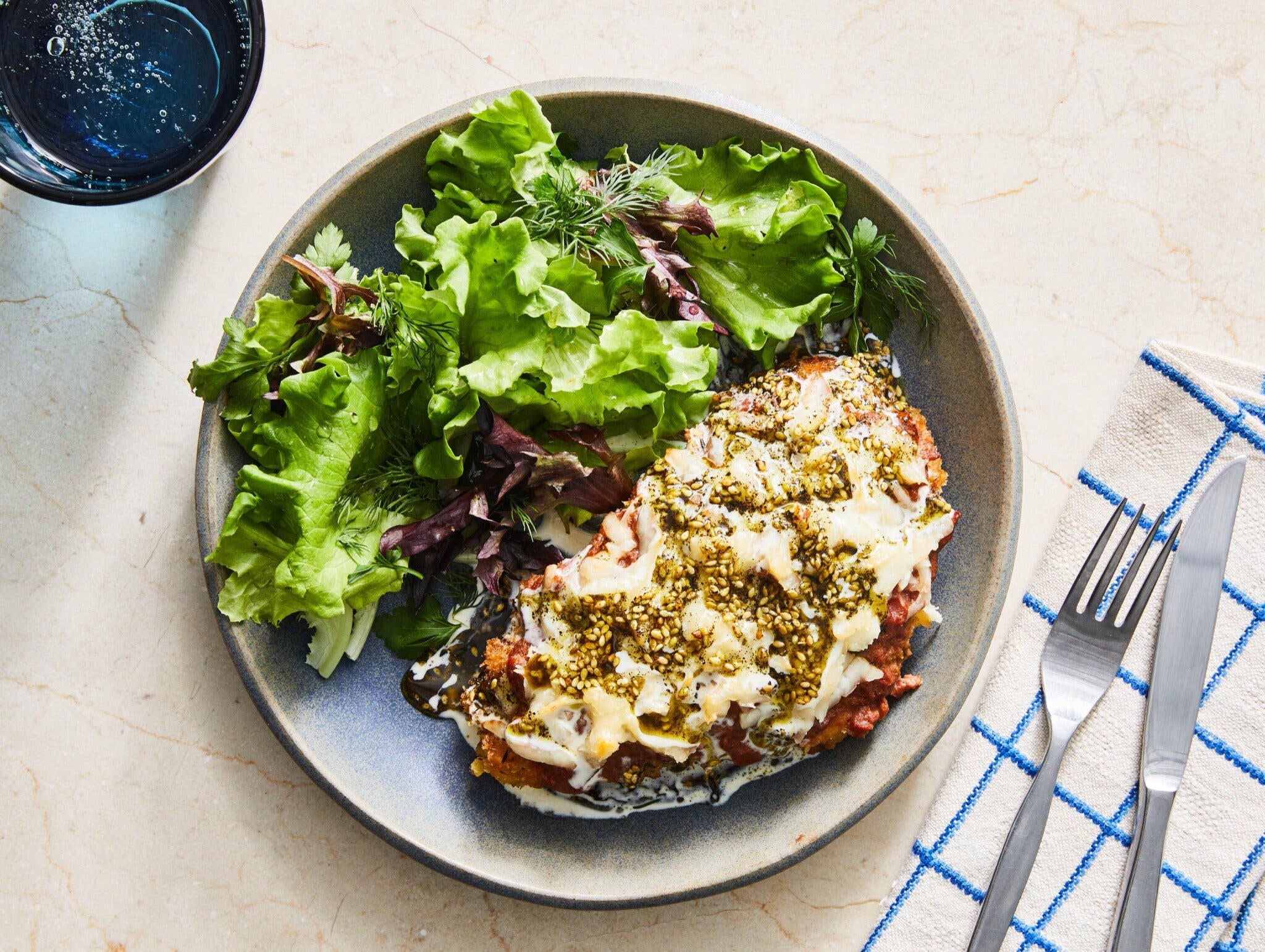 An overhead image of chicken topped with melted halloumi and za’atar next to a green salad.