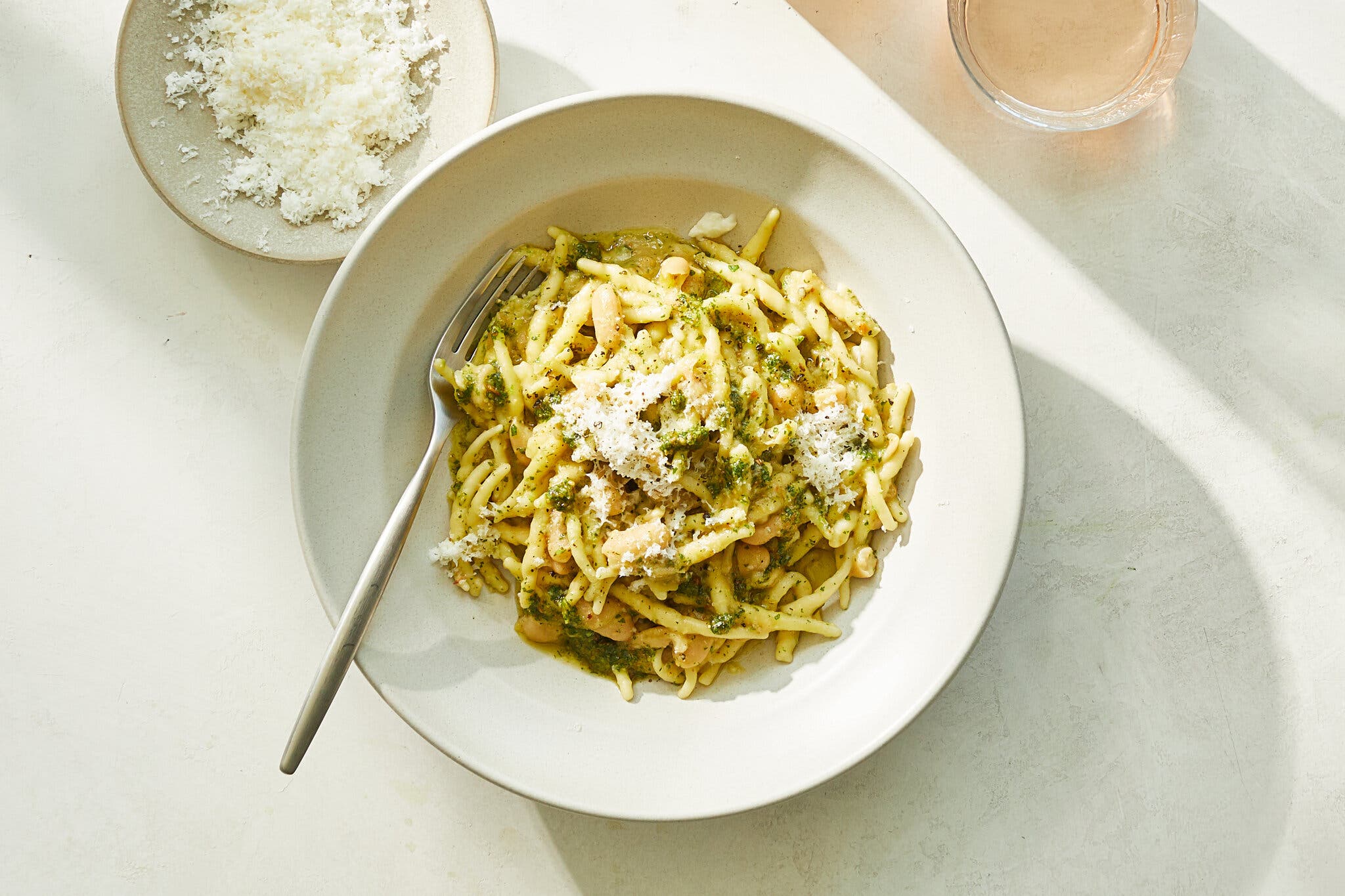 An overhead image of pasta in a wide-rimmed bowl tossed with creamy white beans and grated cheese.