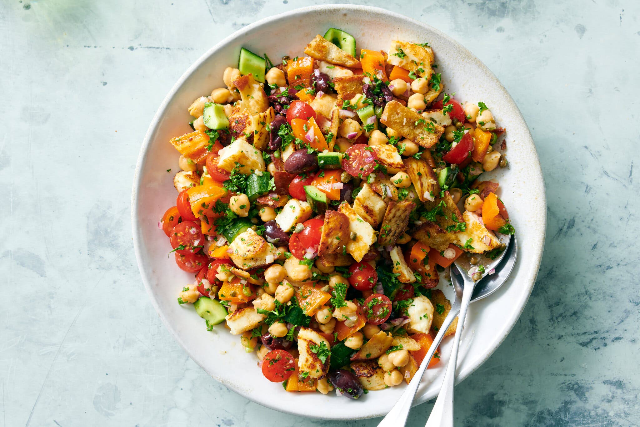 Cubed halloumi, chickpeas and tomatoes are tossed together and photographed on a large platter.