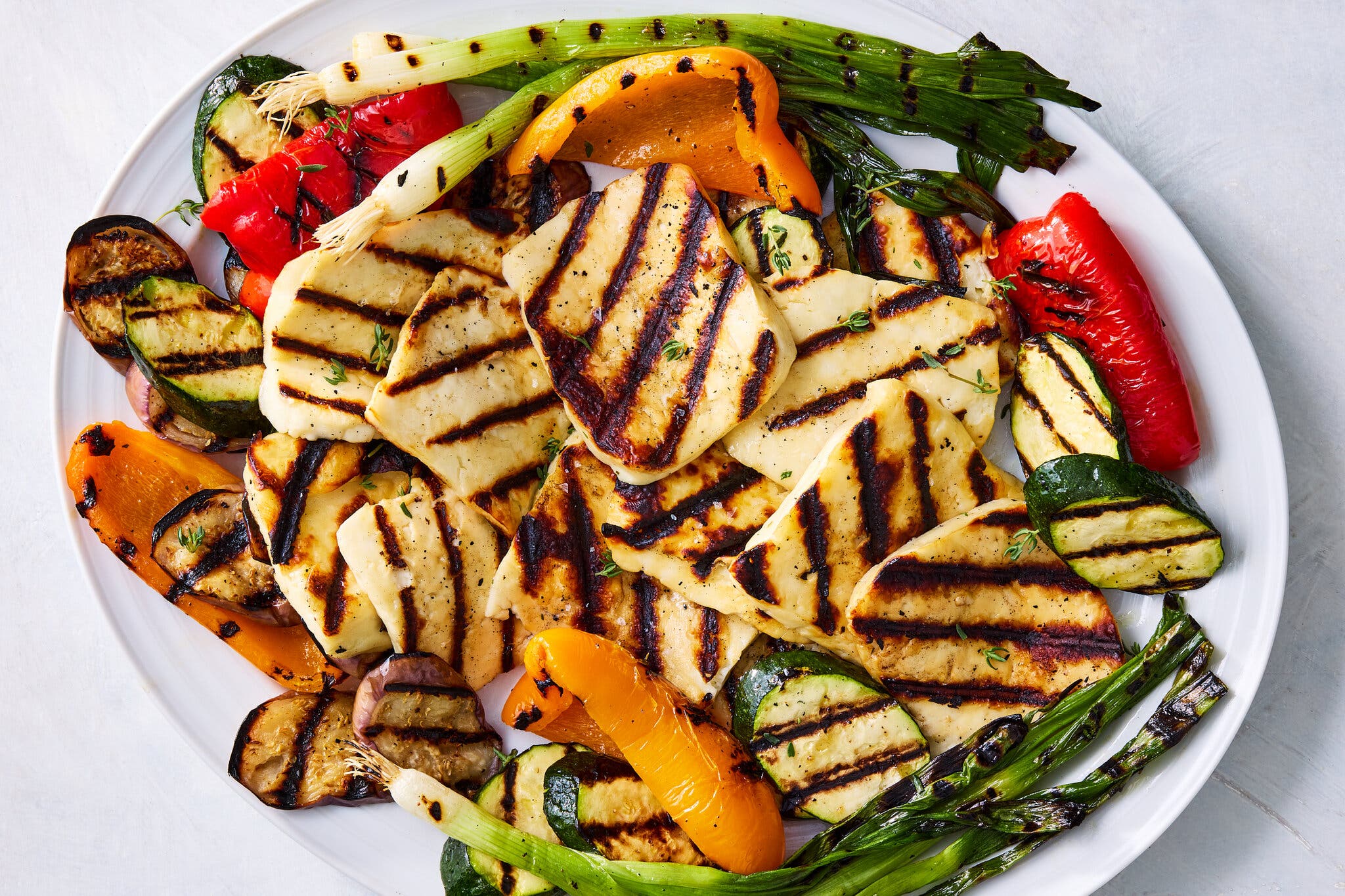 Slabs of halloumi with grill marks lay on a bed of grilled mixed vegetables.