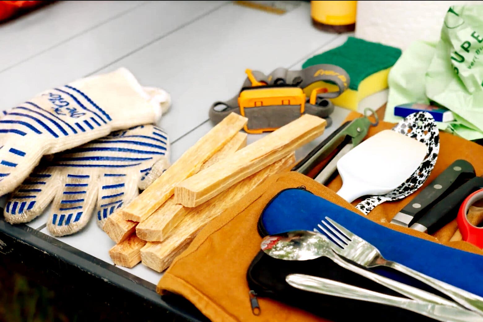 A side image of camp cooking equipment including a headlamp, sponge, utensils and gloves.