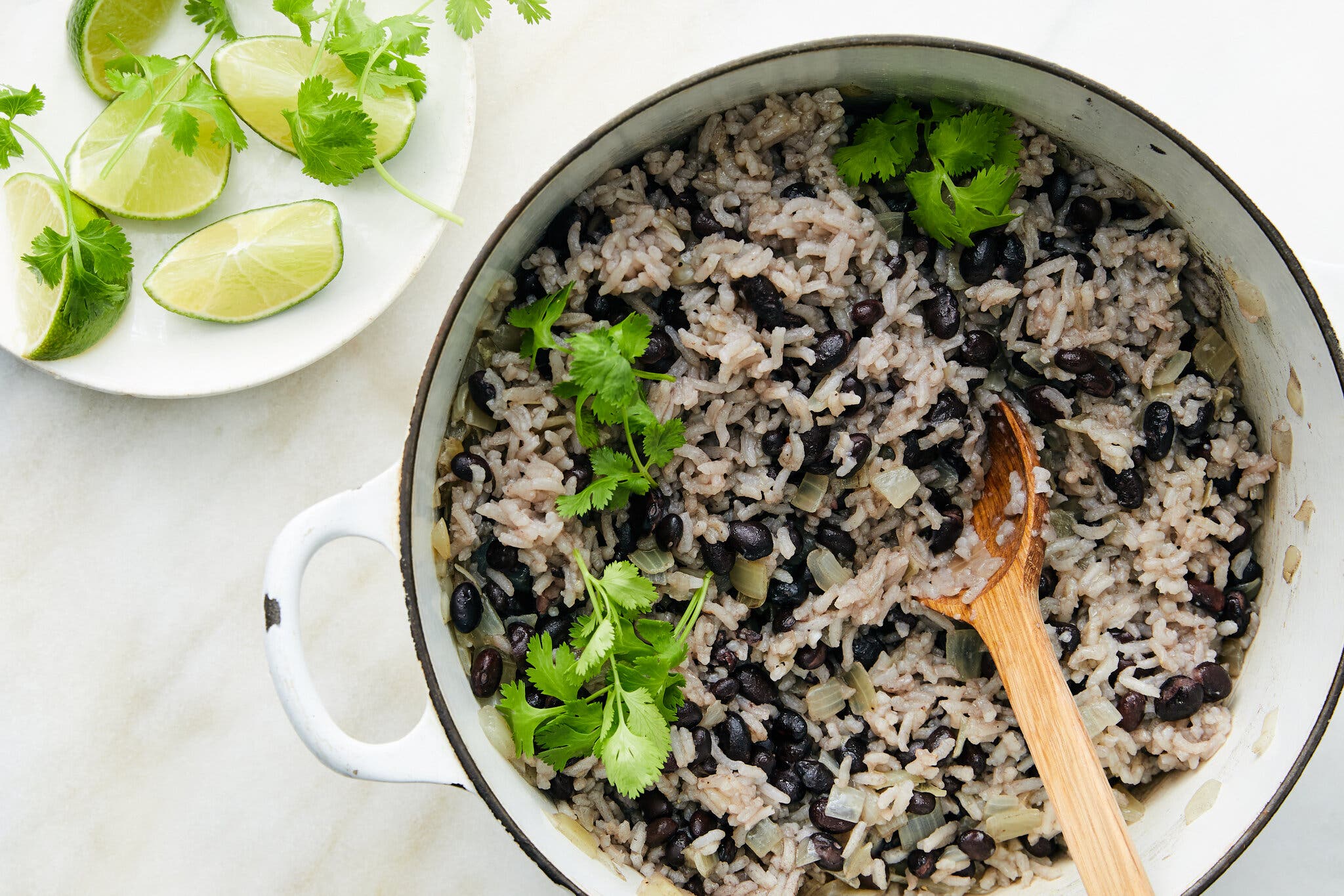 An overhead image of a Dutch oven filled with rice and beans next to a plate topped with lime wedges.