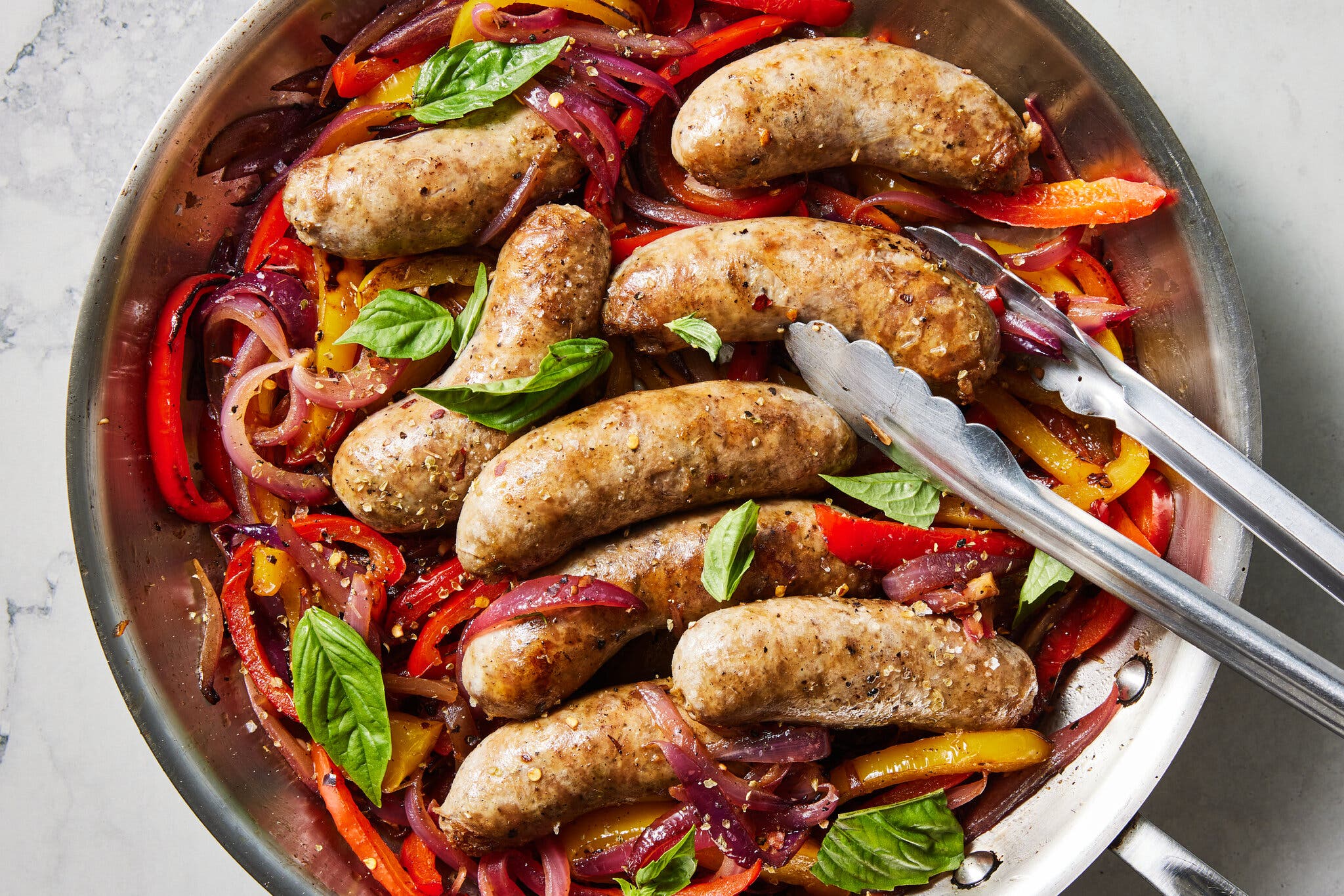 An overhead image of a skillet filled with sausages nestled on a bed of sliced peppers and onions.