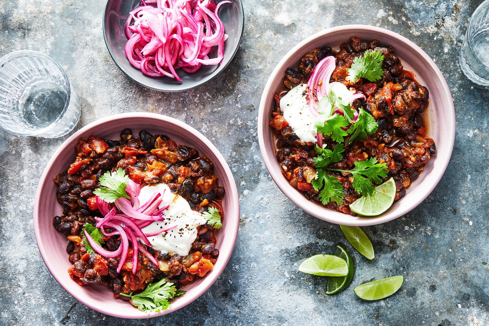 An overhead image of two bowls filled with chili and topped with sour cream and slivered red onions.