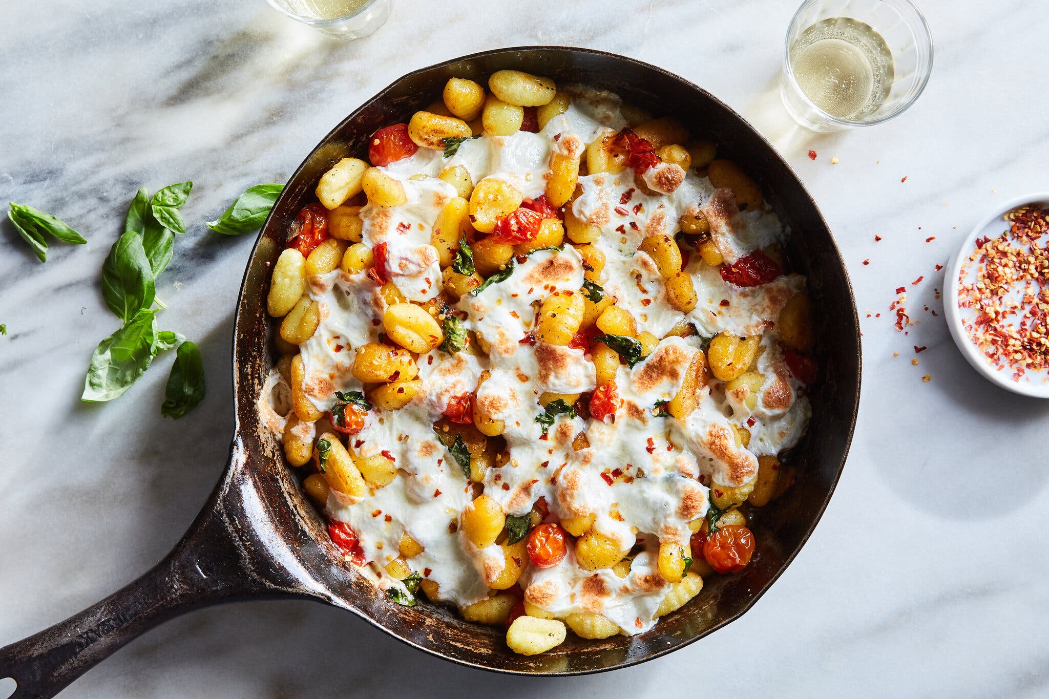 An overhead image of a cast-iron skillet filled with cheesy gnocchi with cherry tomatoes.