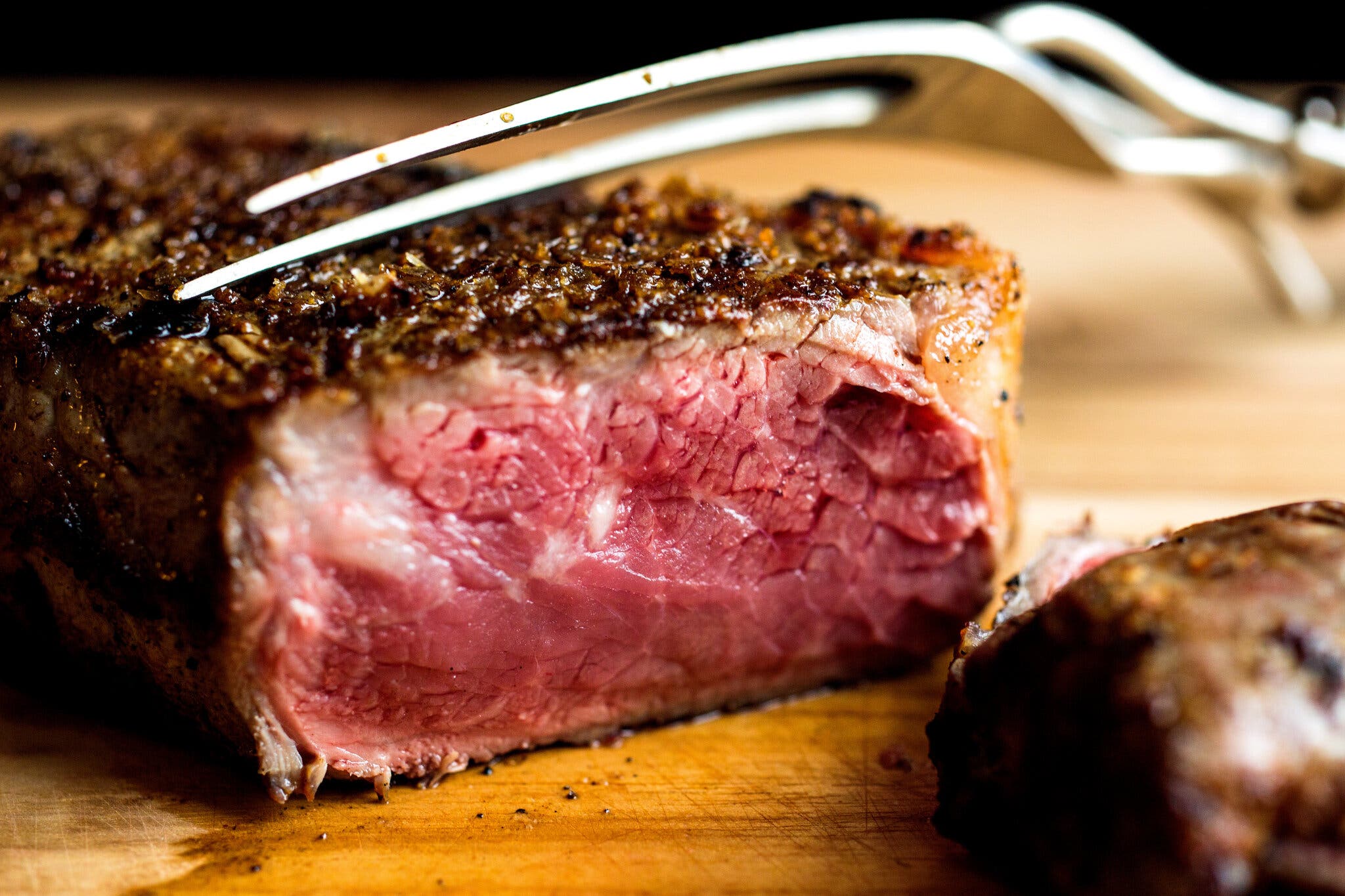 A cross-section of a medium-rare steak is cut into with a serving fork.