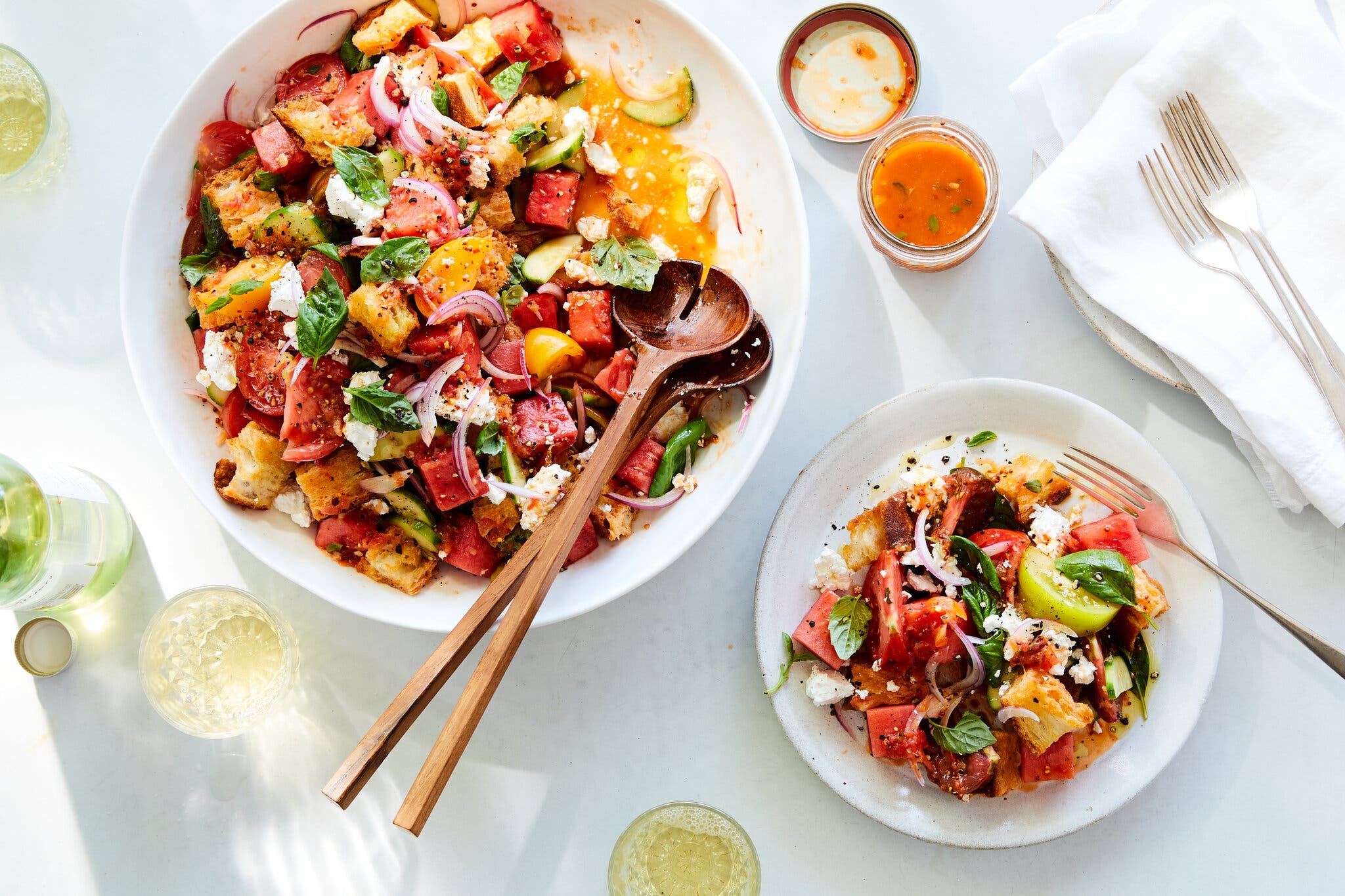 An overhead image of a platter and a serving of watermelon panzanella, full of tomatoes and watermelon cubes as well as crusty cubes of bread.