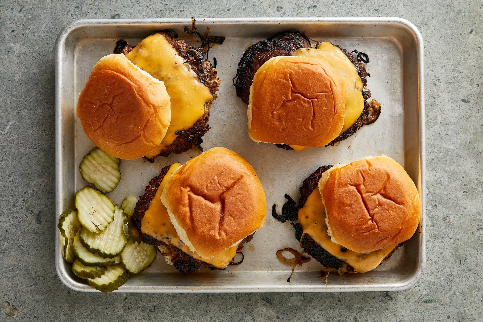 A small rimmed sheet pan topped with four cheeseburgers.
