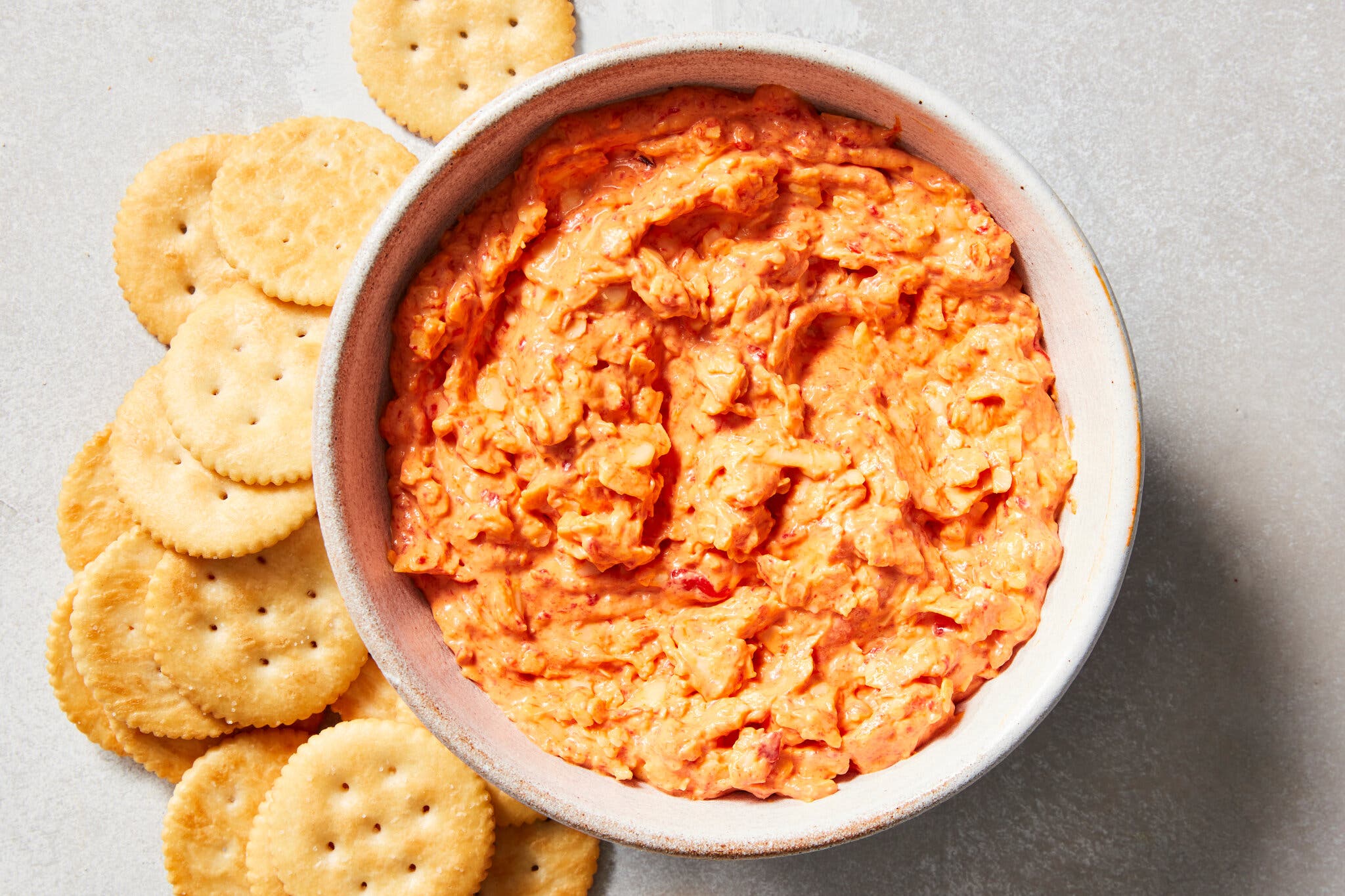 A bowl of pimento cheese with crackers beside it. 