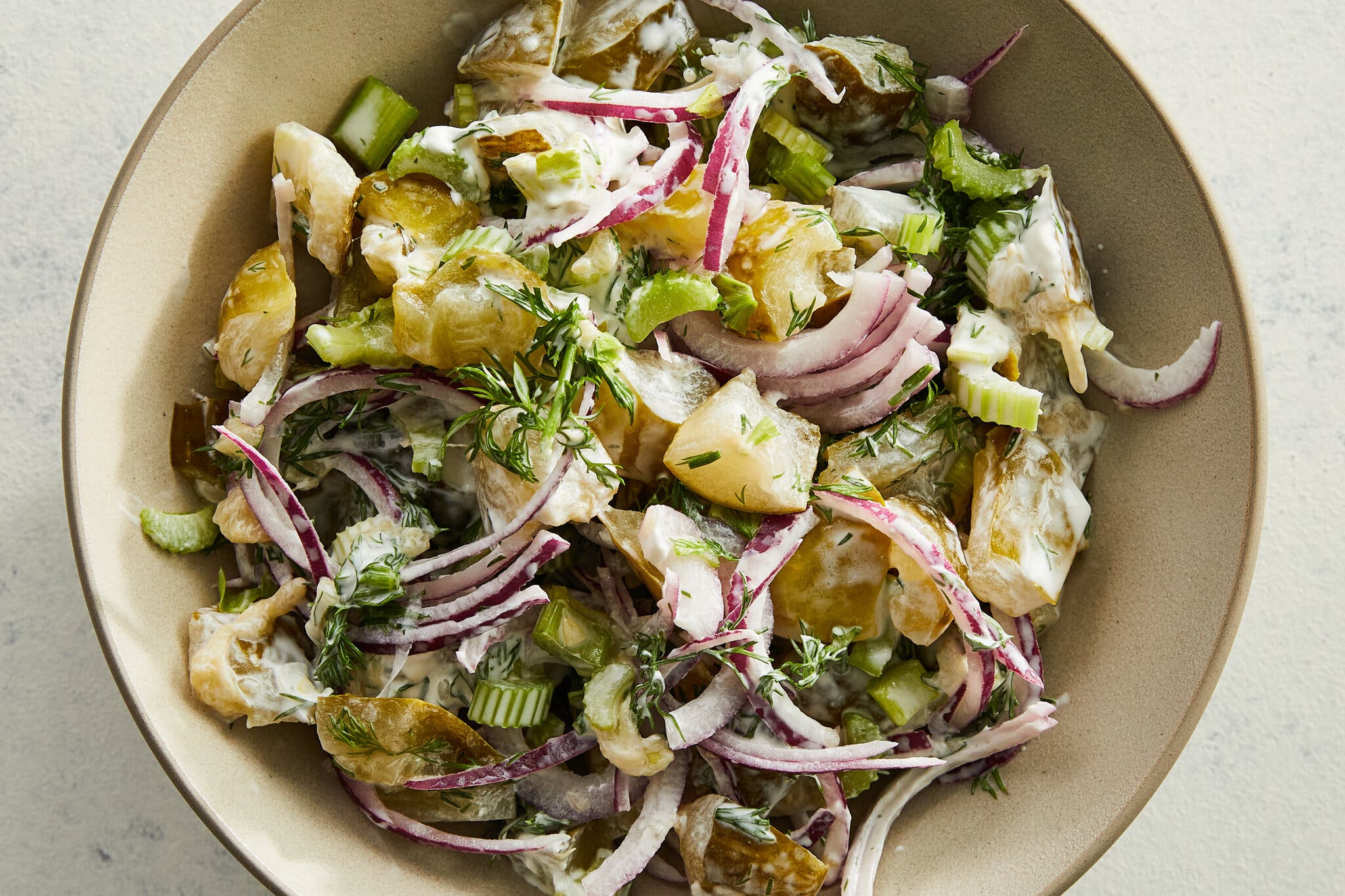 A beige bowl holds smashed pickle salad. 