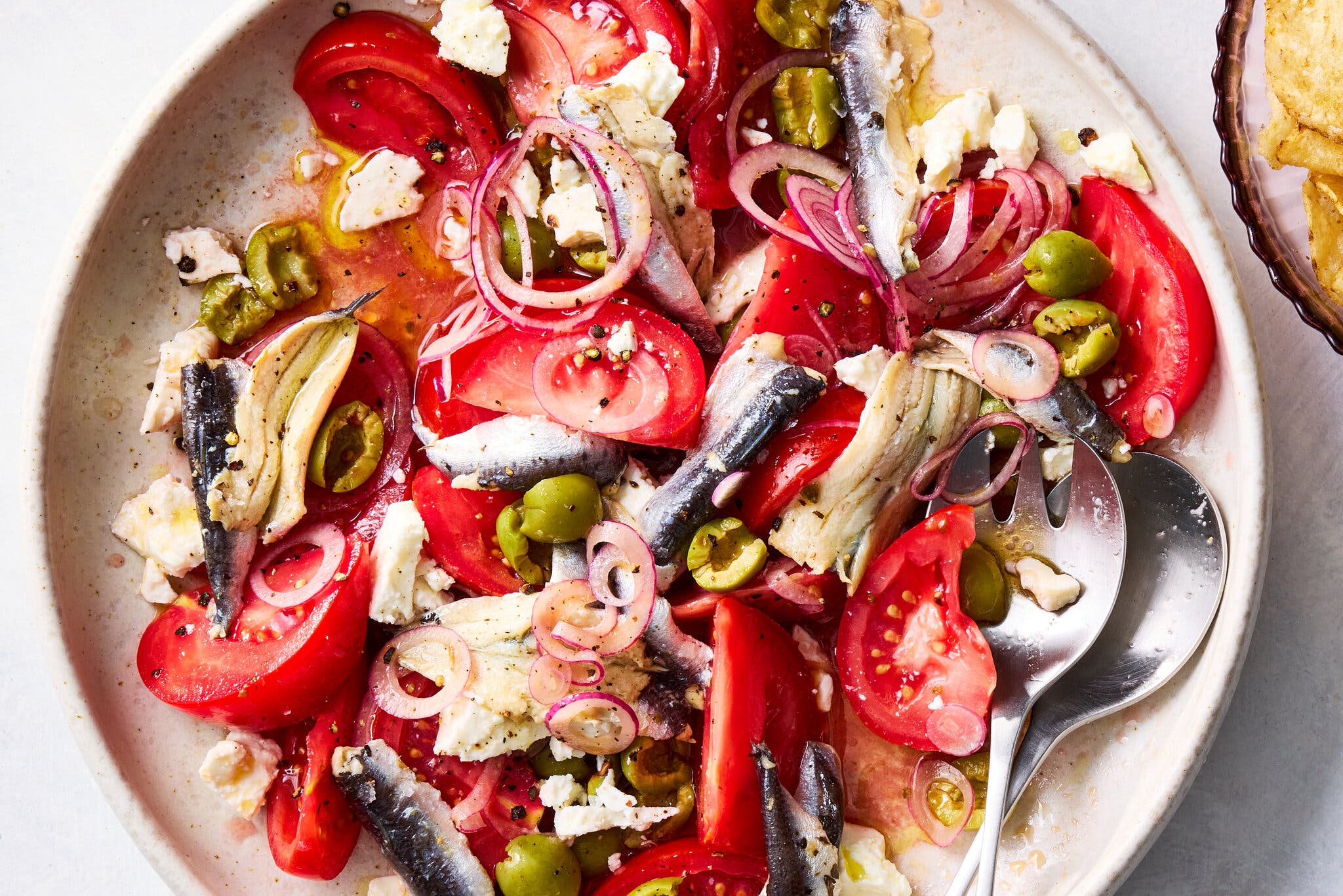A plate of tomato, olive and feta salad with green olives, thinly sliced red onion and tinned fish.