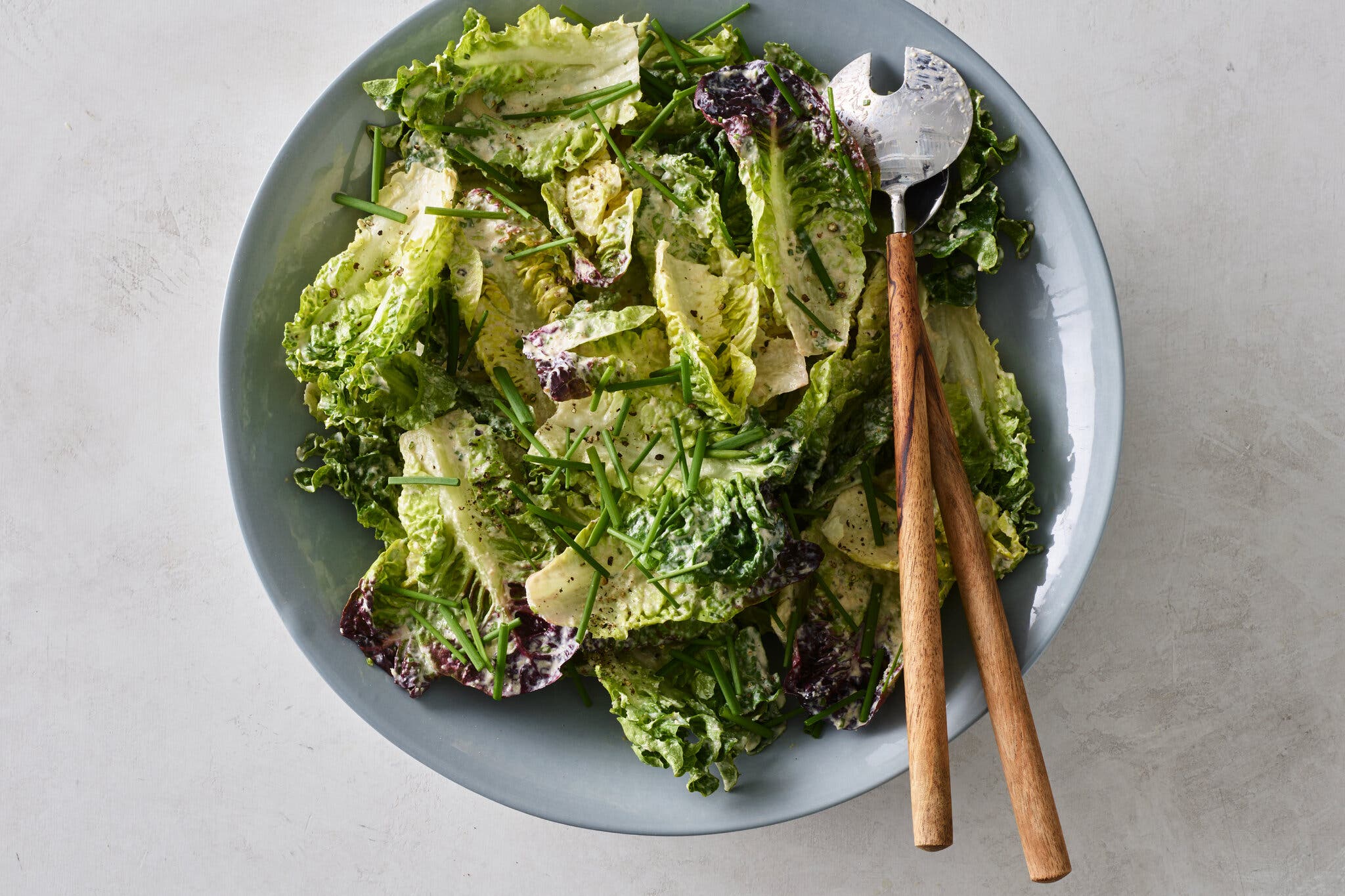 A blue bowl holds a green salad with sour cream and onion dressing and chives sprinkled on top. 