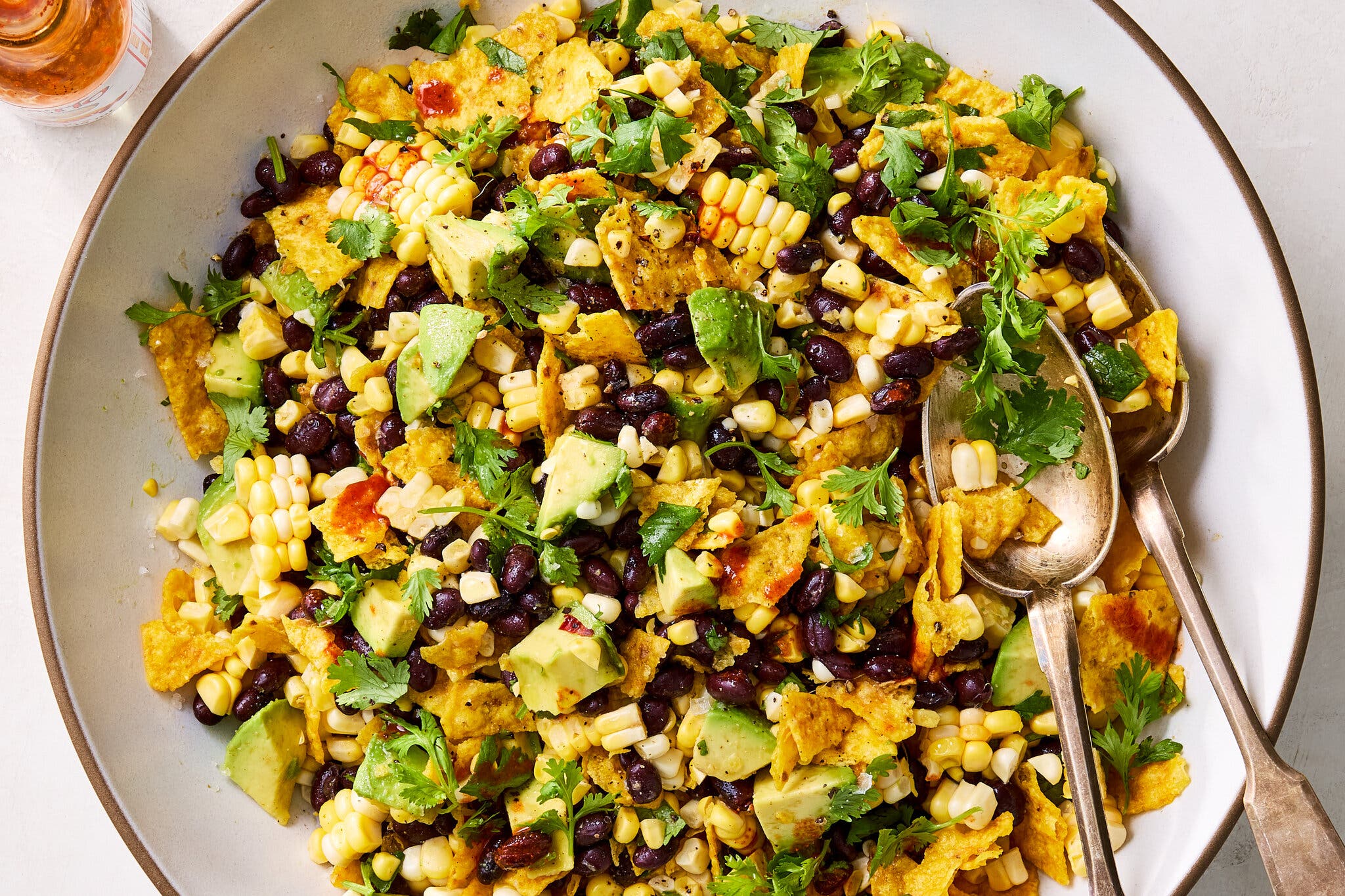 A bowl of corn chip, corn and black bean salad with avocado, topped with hot sauce and cilantro.