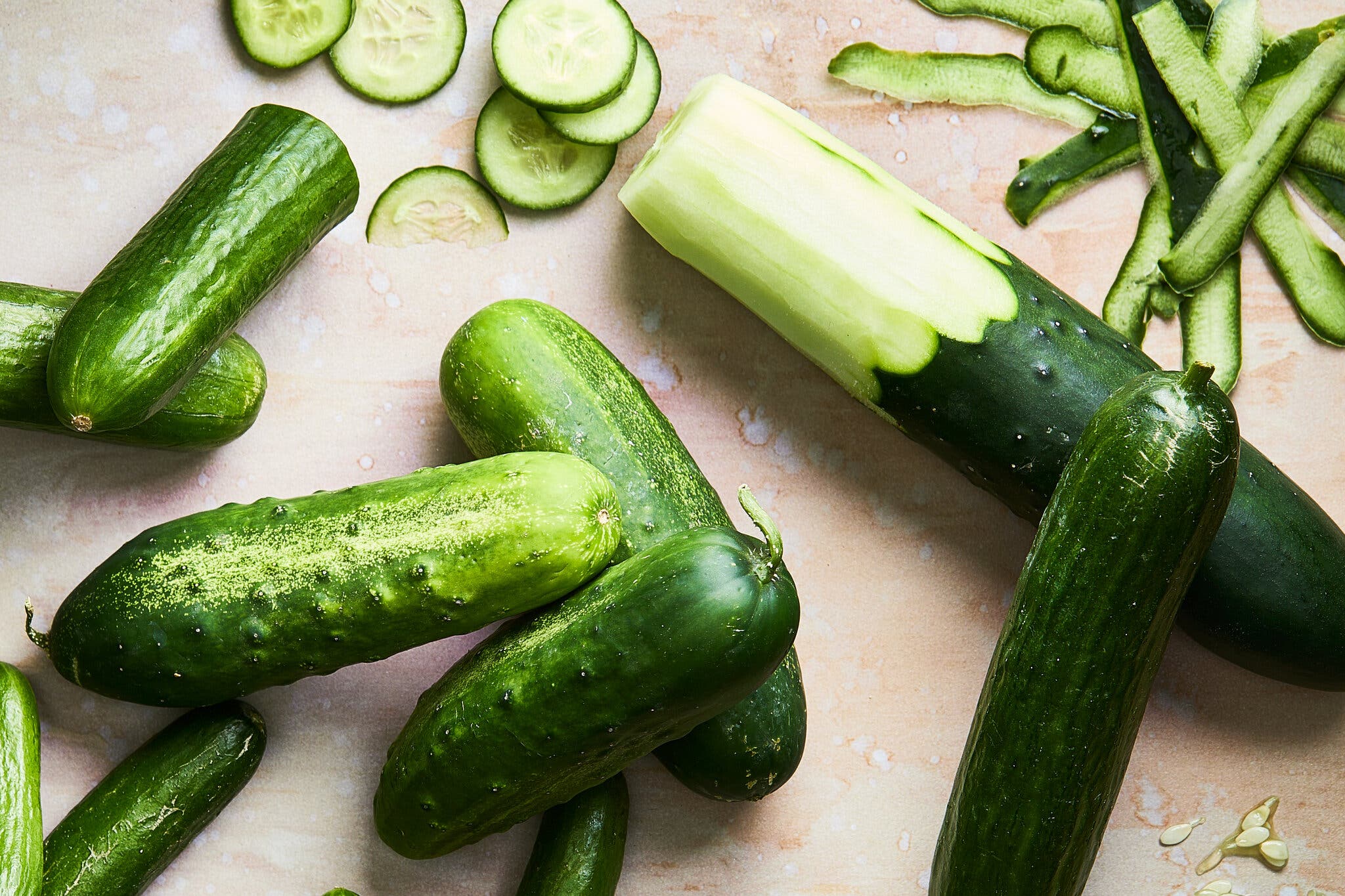 An overhead image of cucumbers. Some are sliced, and others are peeled, with the peel off to the side.