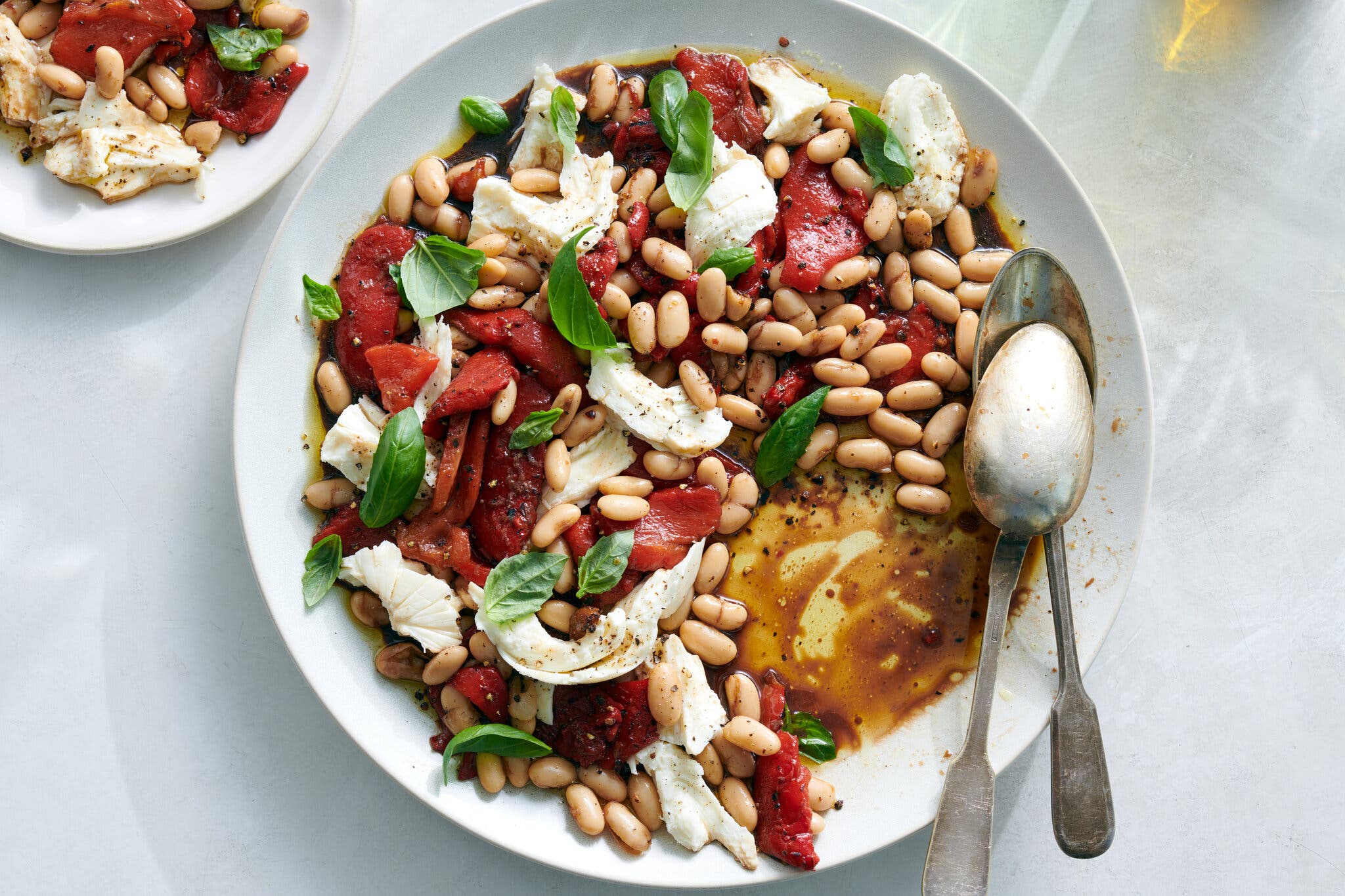 A plate holds roasted red peppers, white beans, mozzarella and basil dressed in olive oil and balsamic vinegar.