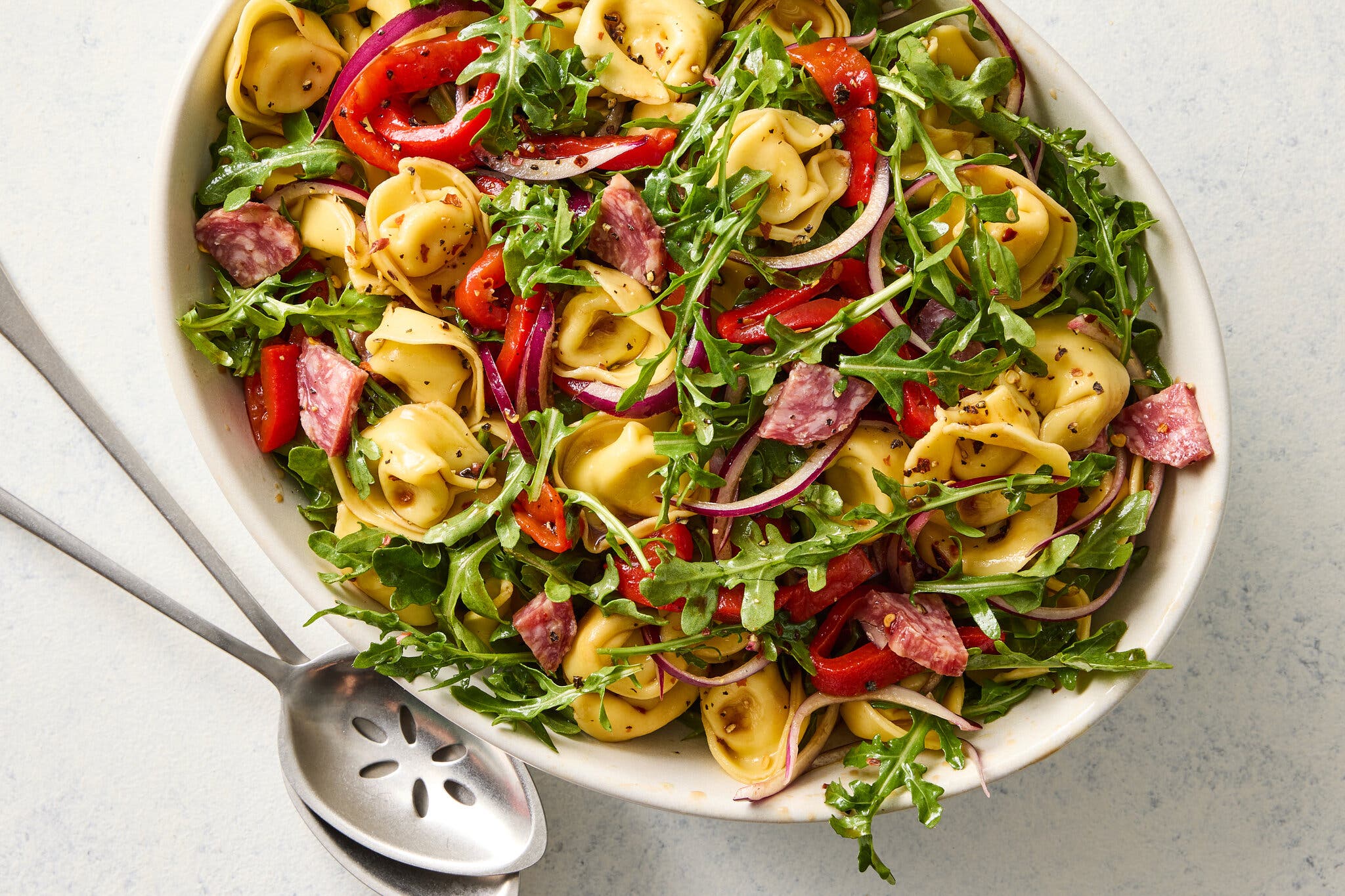An overhead image of tortellini tossed with arugula, peppers and onion.