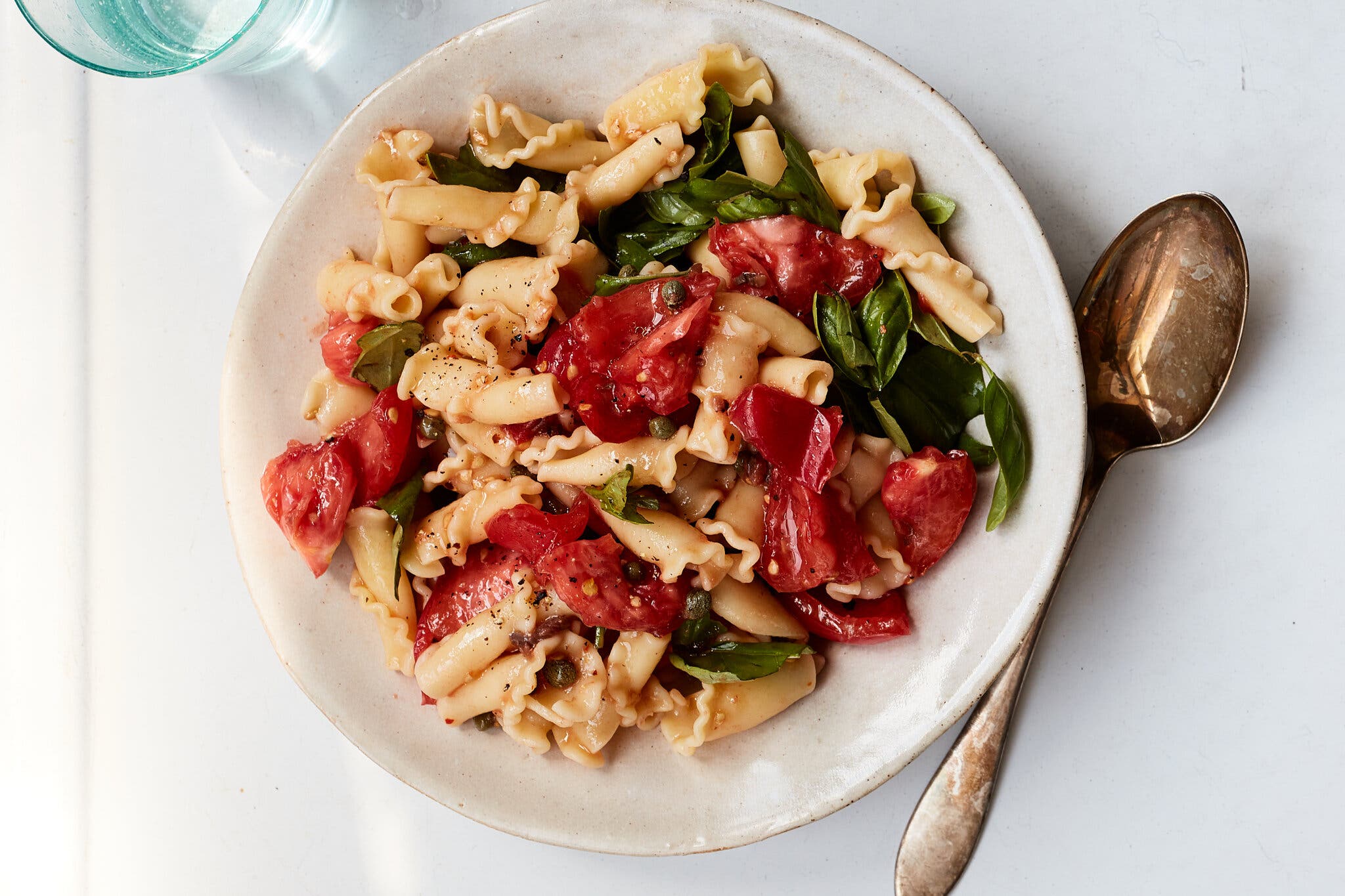 An overhead image of curly pasta tossed with tomatoes and herbs.